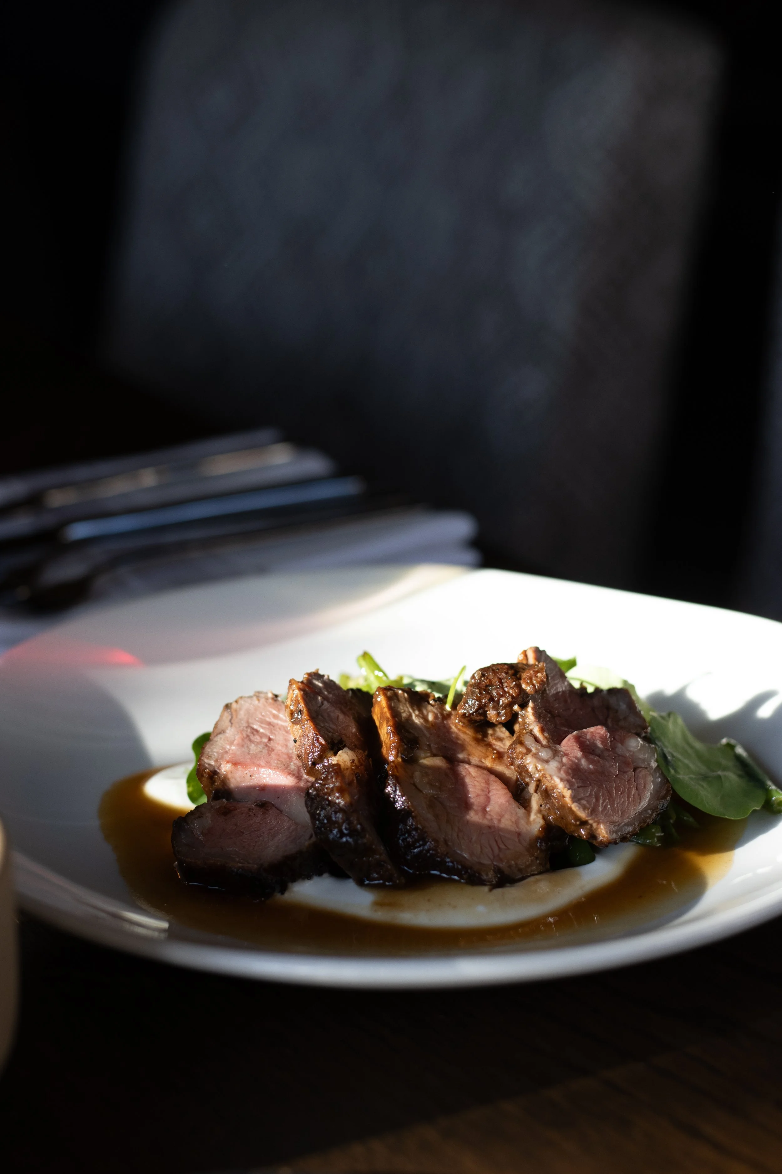 Close-up of a plated gourmet steak dish with sliced beef, greens, and sauce, on a white plate. The Lamb Inn. 