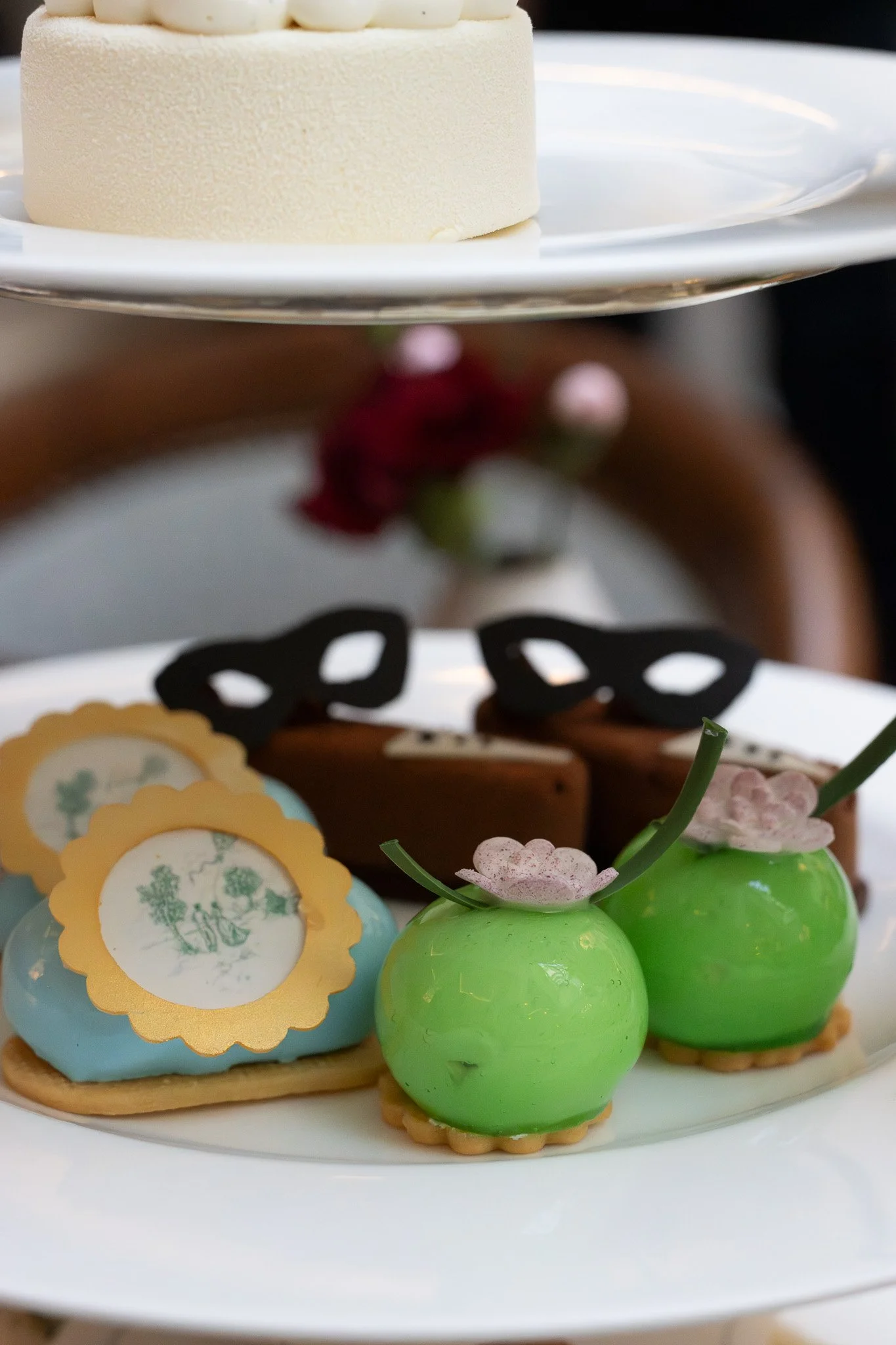 A white plate holding a white frosted cake decorated with white chocolate balls, with various decorated cookies and green and pink chocolate bunny figures around it.  The Lanesborough. Bridgeton Afternoon Tea.
