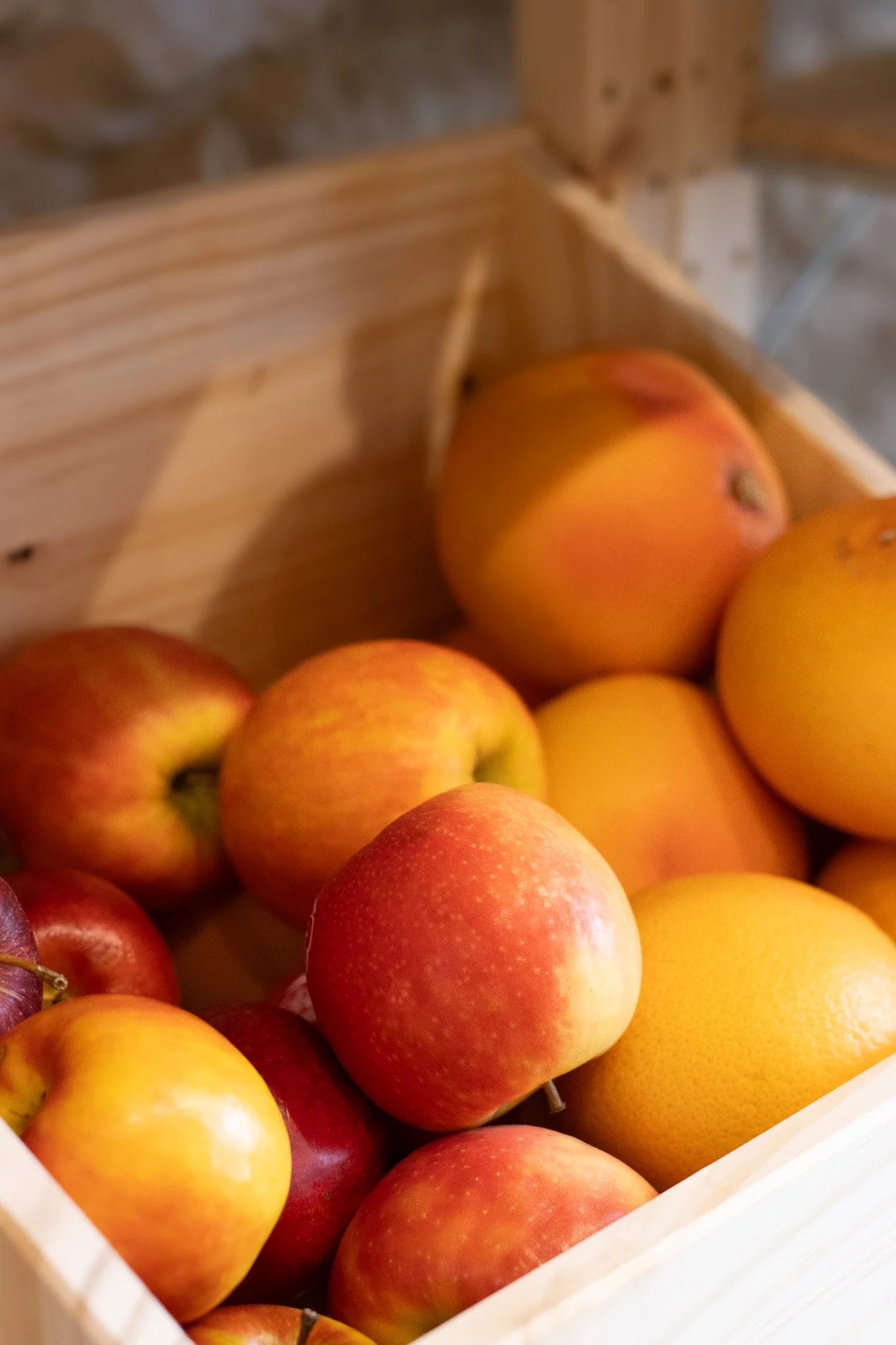 A wooden box filled with fresh apples in various shades of red, yellow, and orange. The Cotswold Farm. 