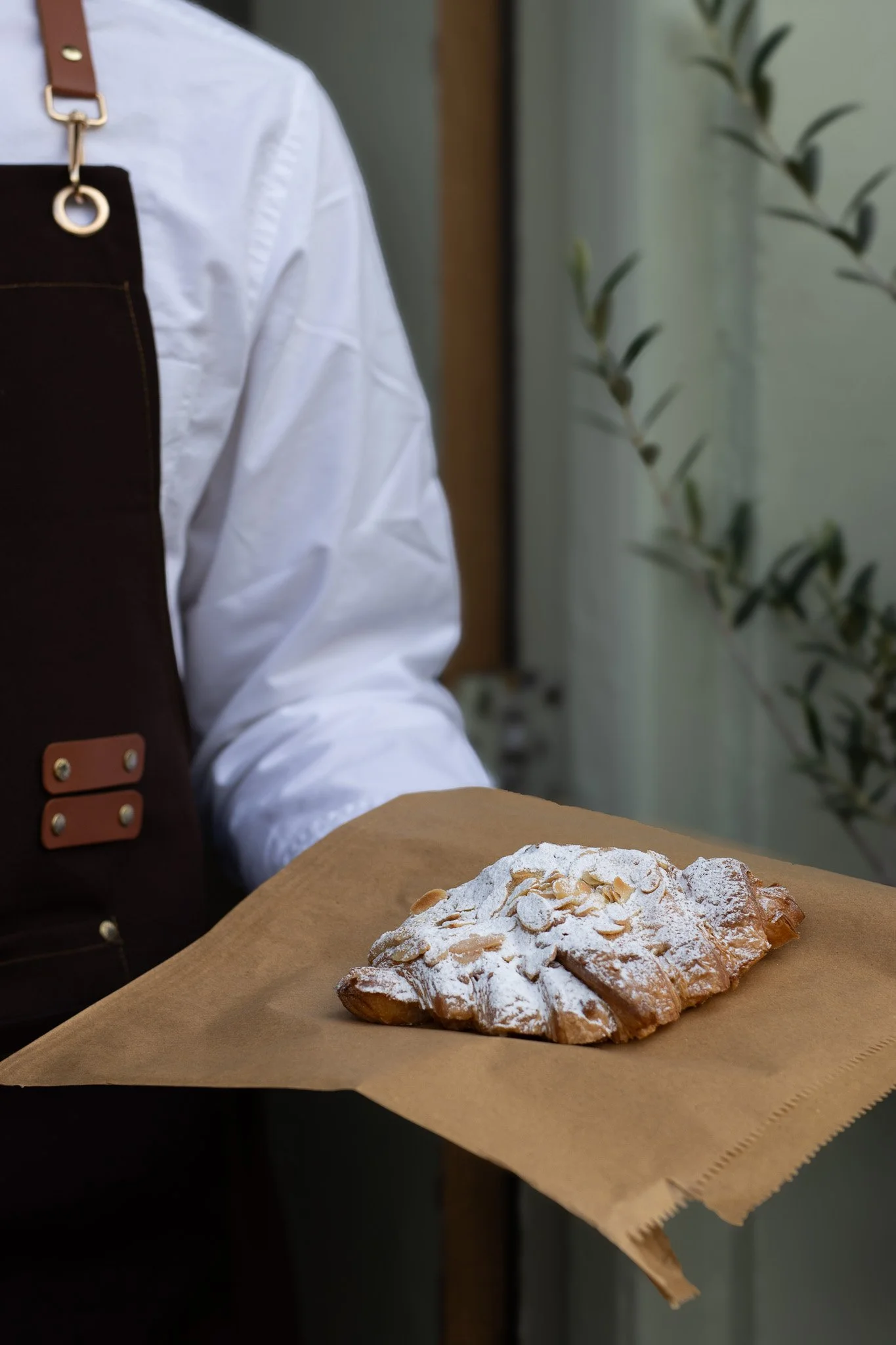 A pastry dusted with powdered sugar and sliced almonds on a brown paper-wrapped tray. The Cotswold Farm. 