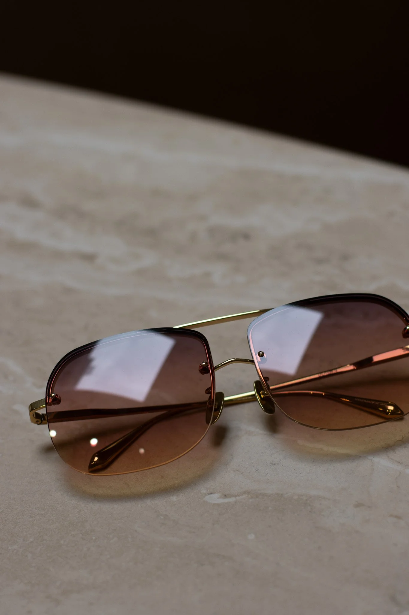 A pair of sunglasses with rose gold frames and tinted lenses resting on a white surface. Linda Farrow.