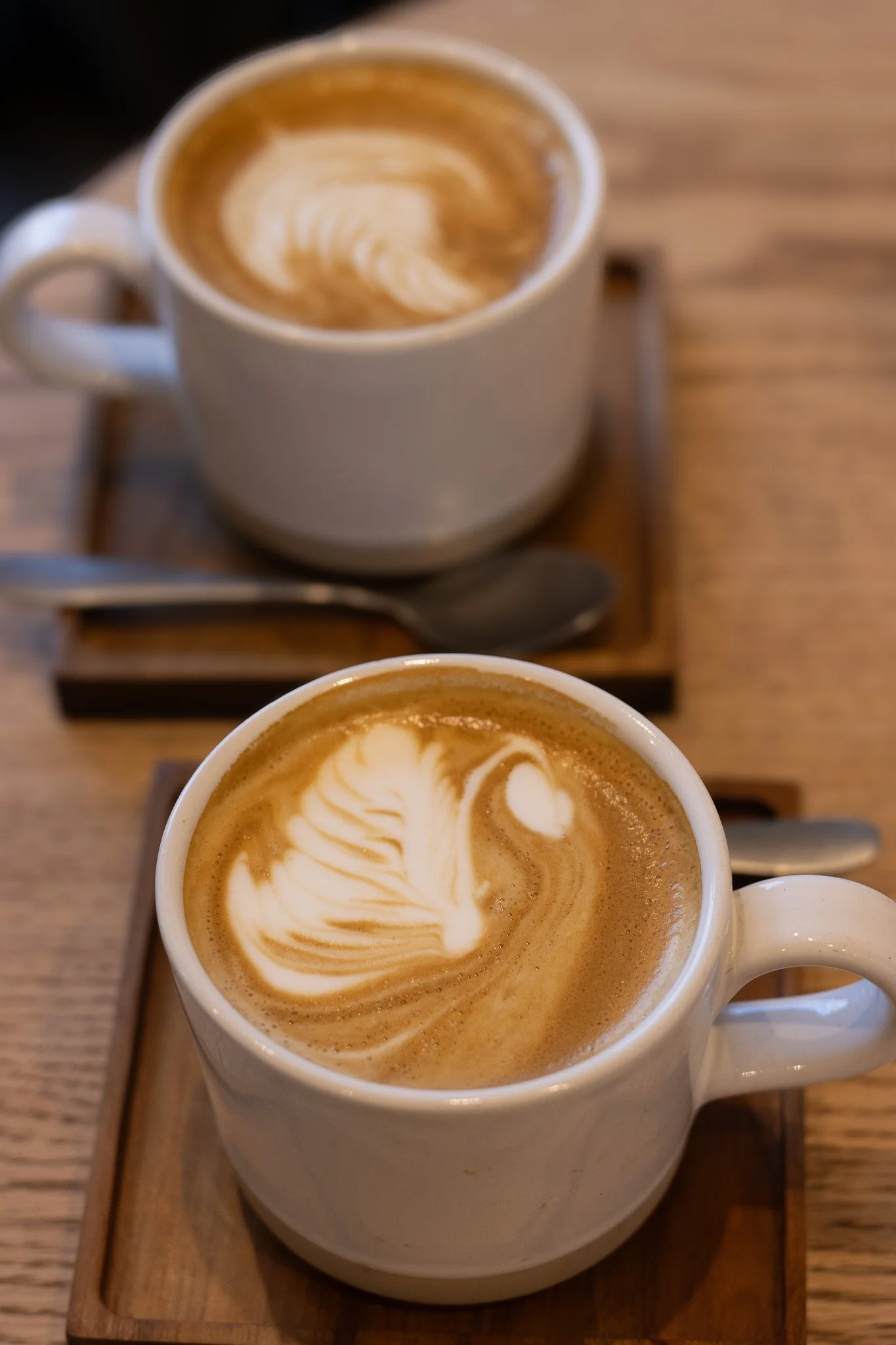 Close-up of two cups of latte with latte art, placed on a wooden tray on a wooden table. The Cotswold Farm. 