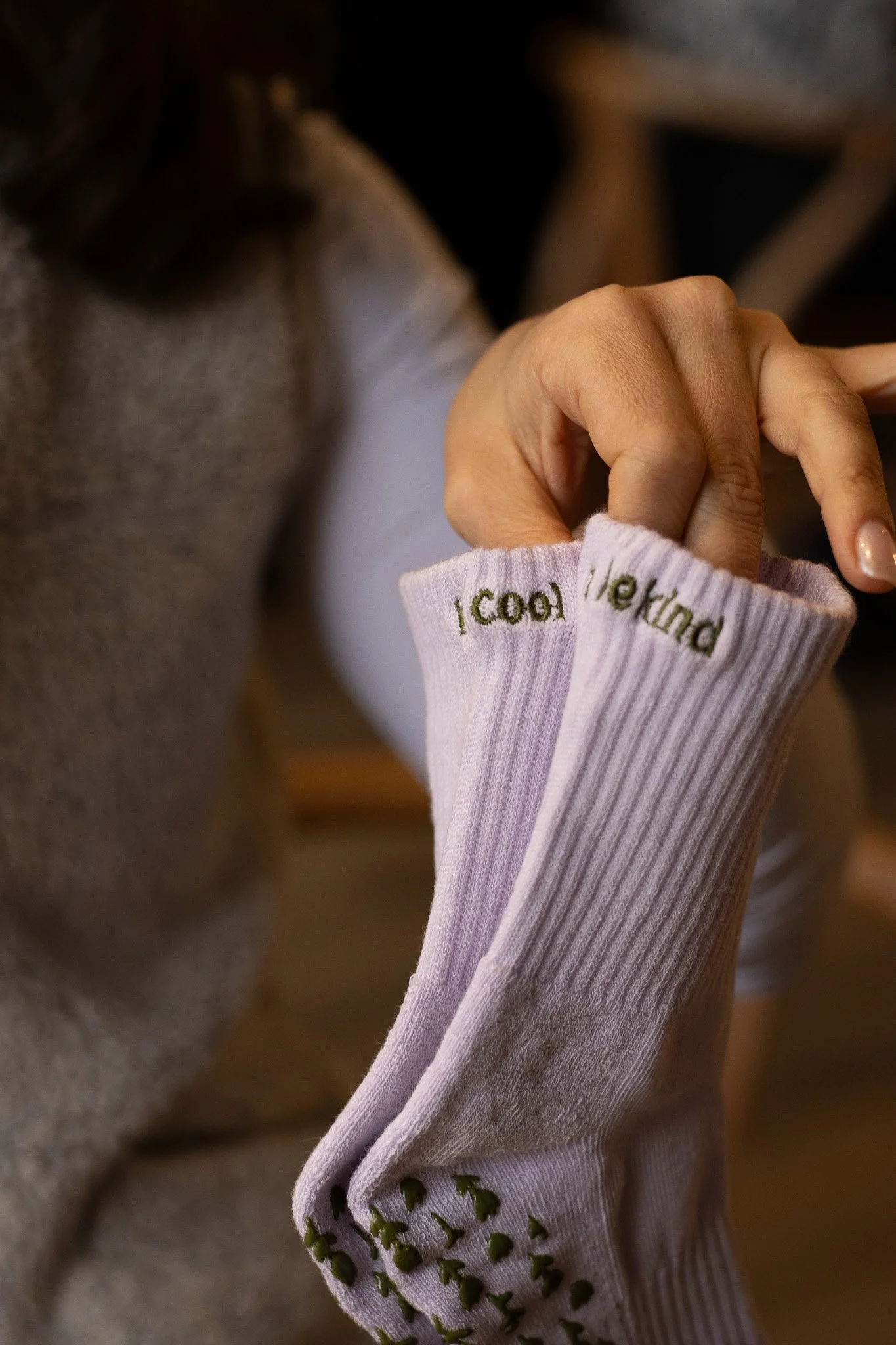 Close-up of a woman's hand with a pink long-sleeve shirt featuring embroidered green text and designs. She is touching her face with the other hand, and her brown hair is partially visible. GetAGrip Apparel. 