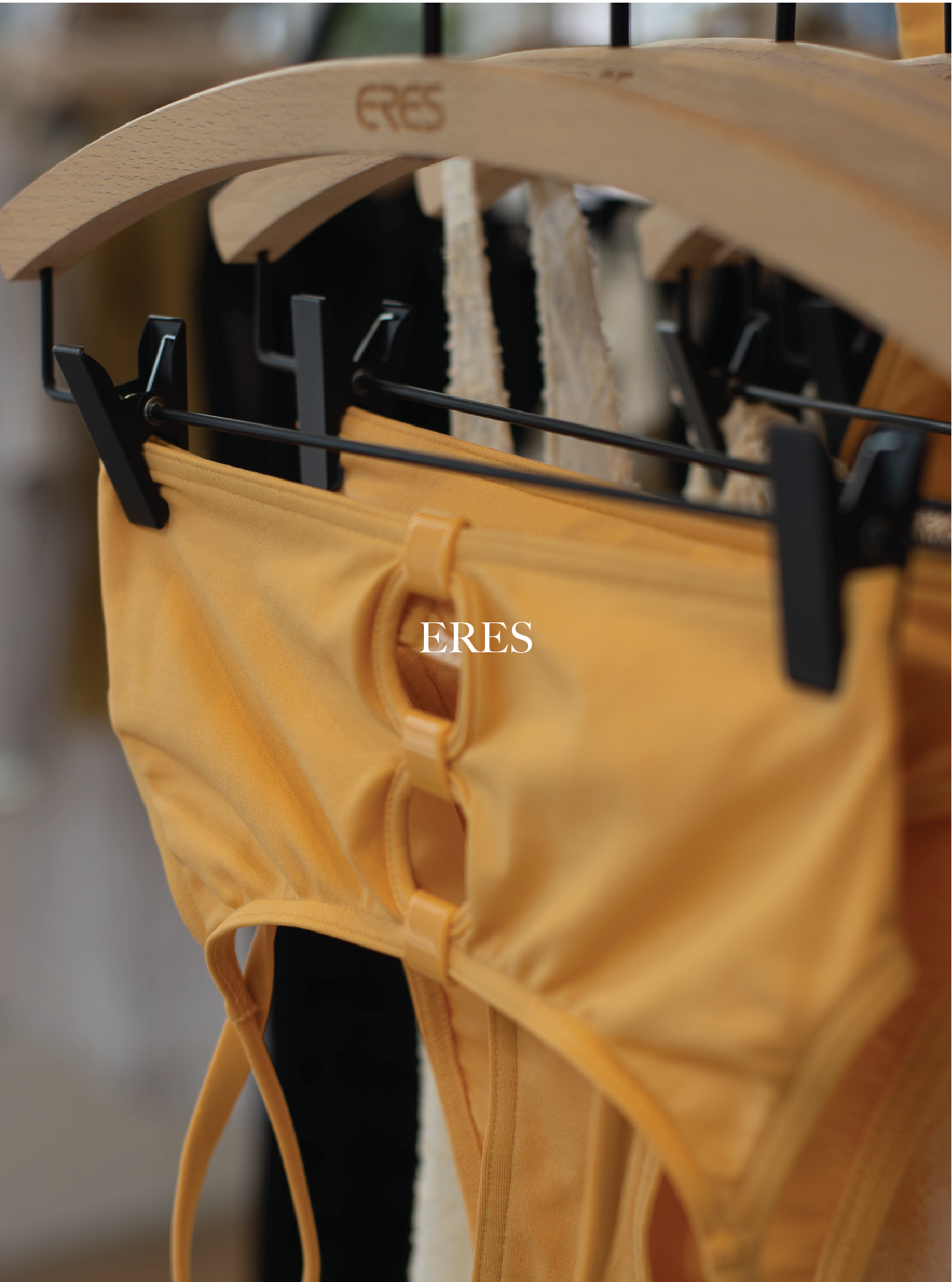 Yellow clothing item hanging on a hanger with black clips, underneath a wooden hanger with the word 'ERES' engraved on it. ERES.