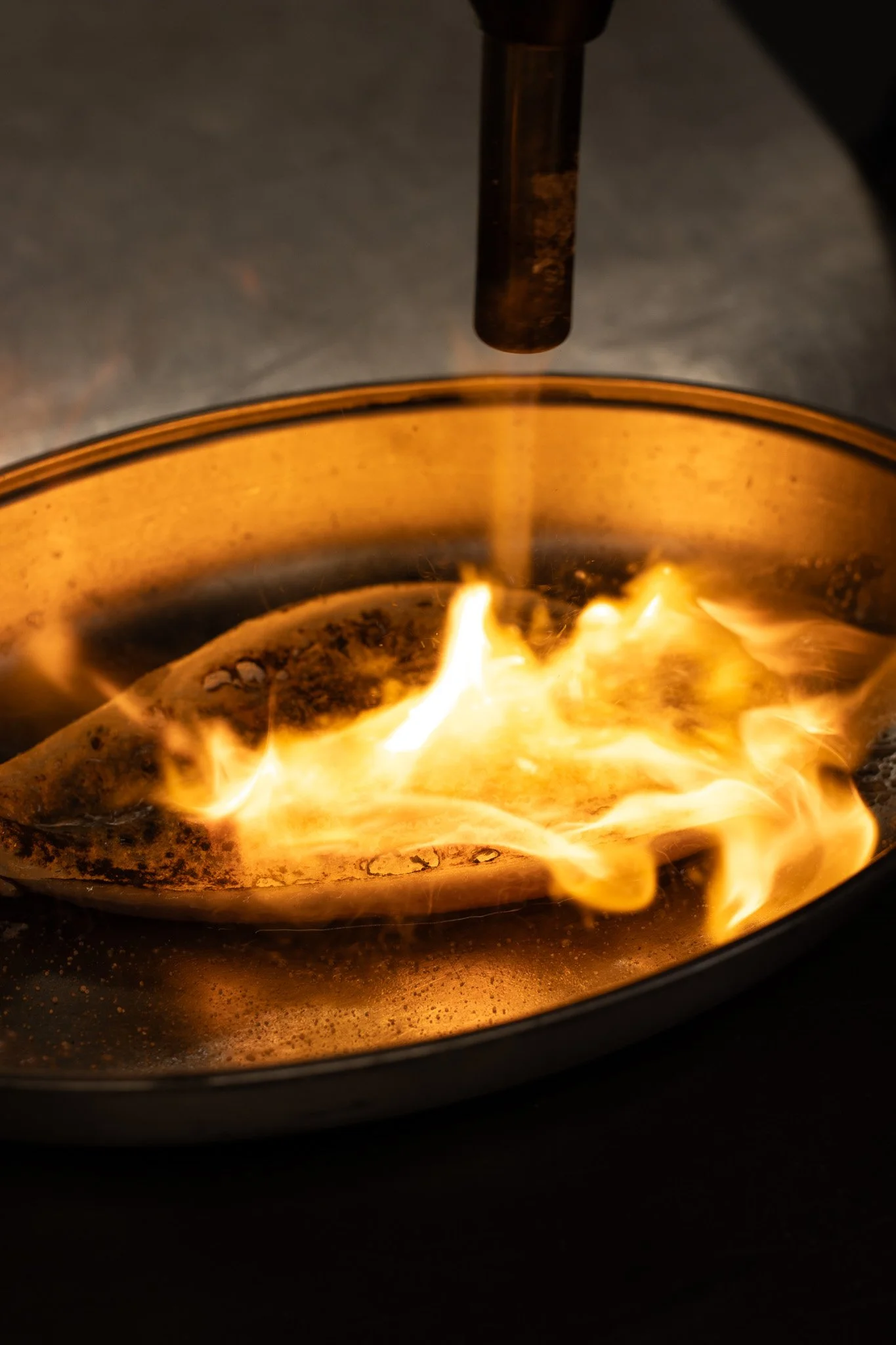 A close-up of a wood-burning stove with a visible flame and a metallic pipe above it. The Lamb Inn. 
