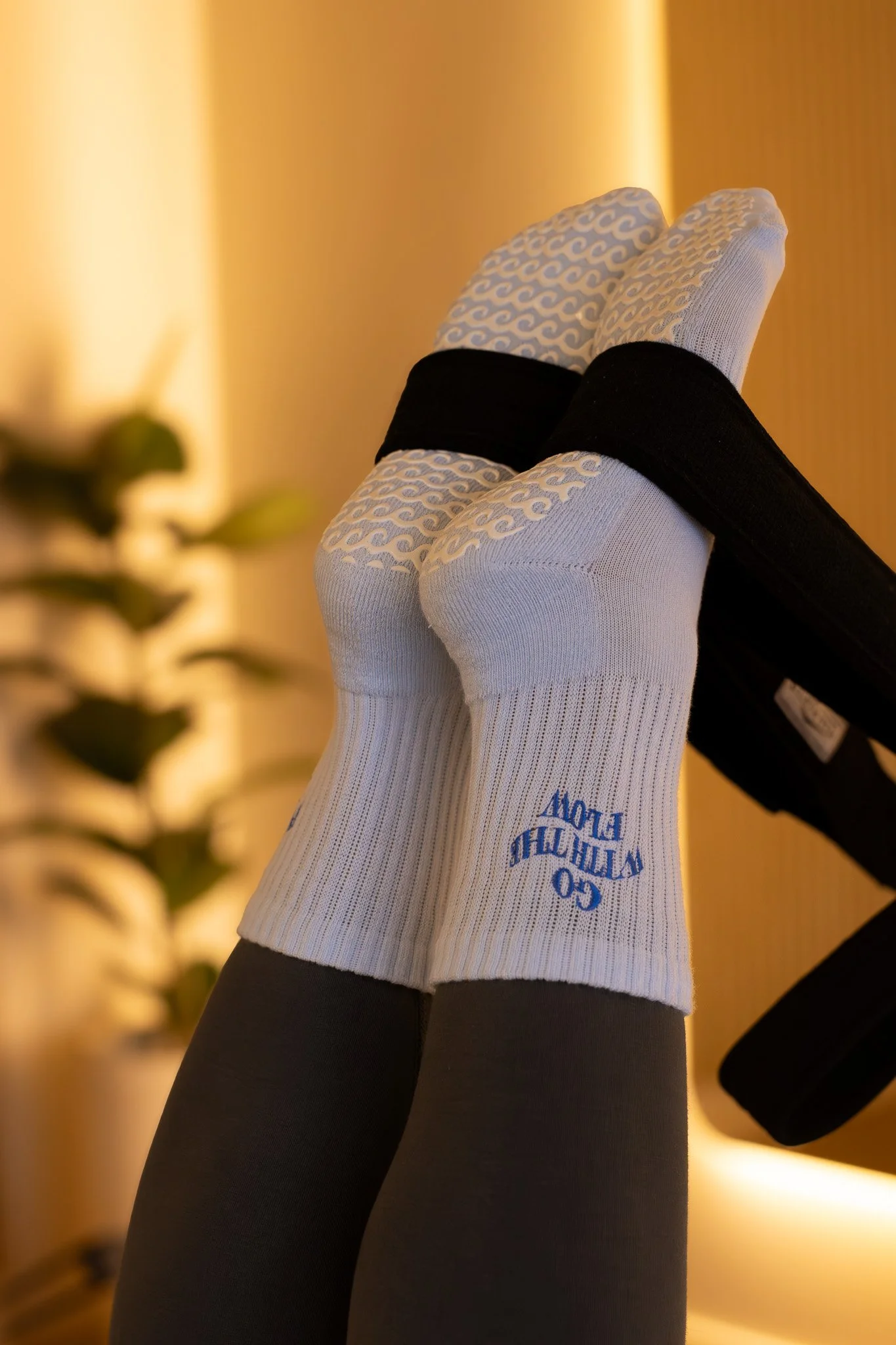 Display of white athletic socks with blue logo, worn with black leggings, against a warm-toned background. GetAGrip Apparel. 