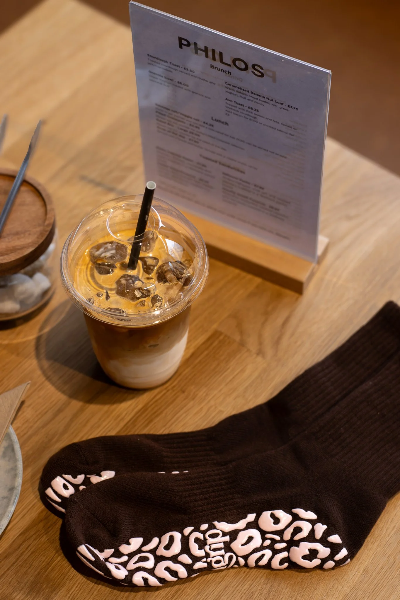 A plastic cup of iced coffee on a wooden table in front of a menu stand, with a leopard print hoodie partially visible in the lower part of the image. GetAGrip Apparel. 