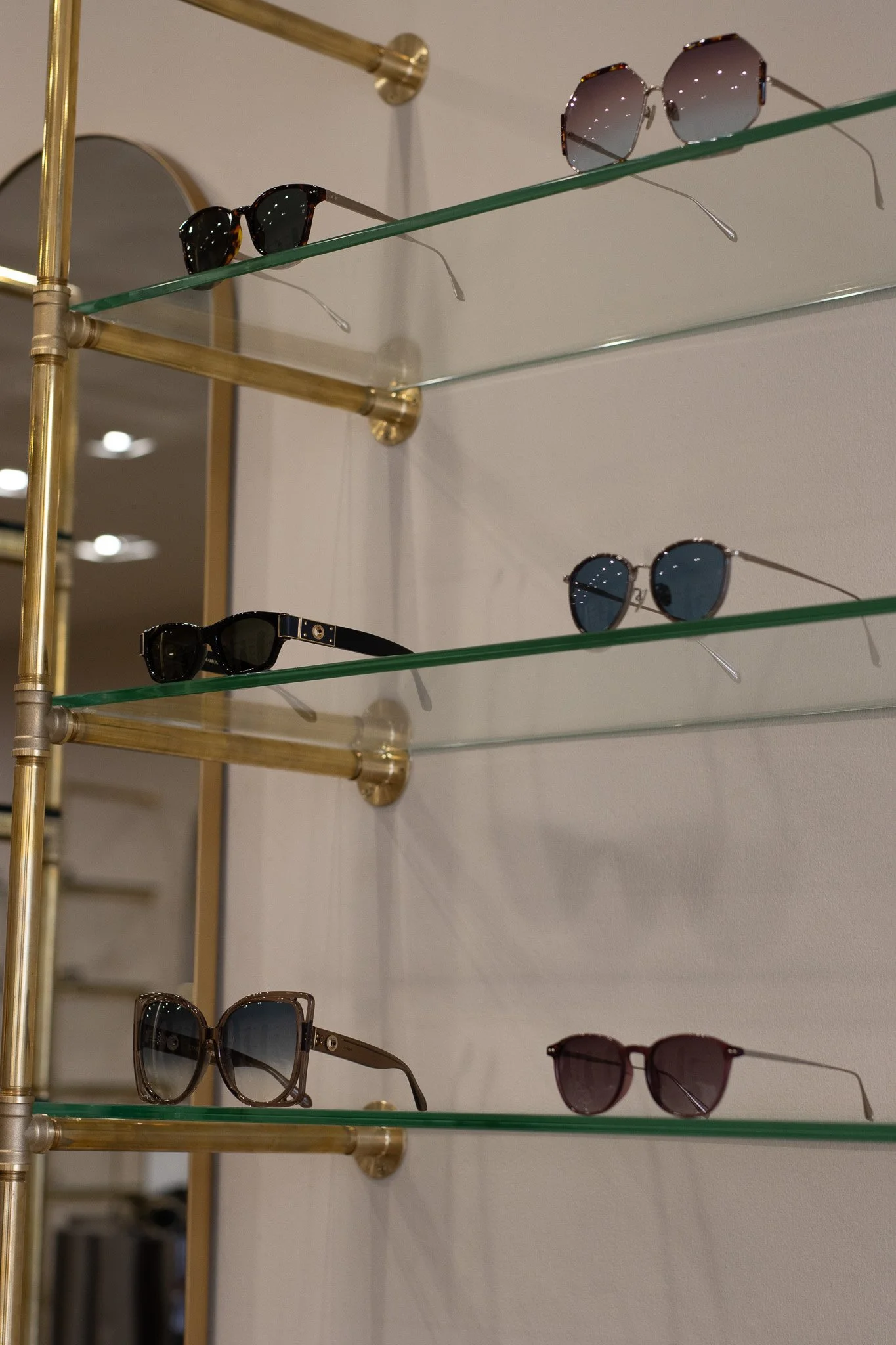 Display of sunglasses on glass shelves with gold-colored metal frame. Linda Farrow.