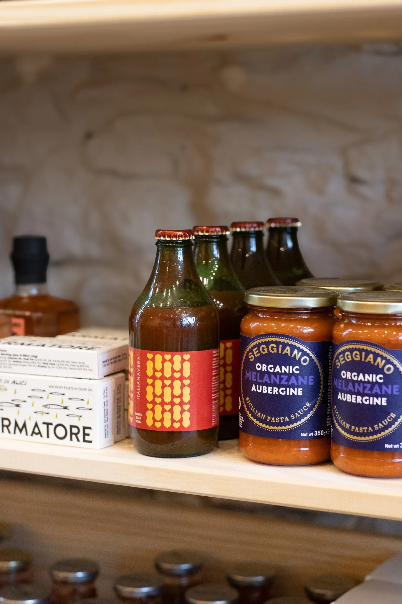 Assorted food products on a shelf including jars of organic eggplant and aubergine pasta sauce, bottles of Italian vegetarian beverage, and boxes labeled with various food items. The Cotswold Farm. 