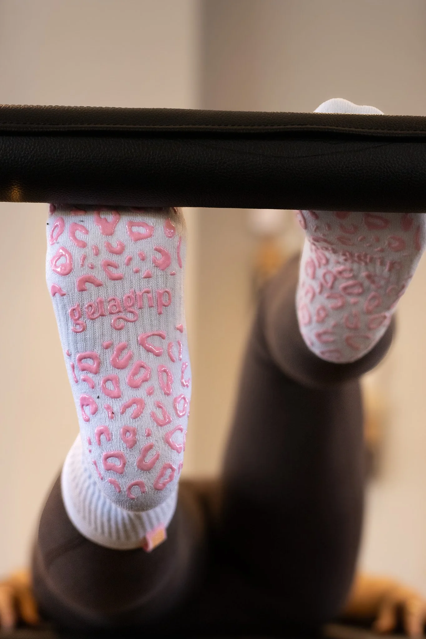 Close-up of a person's feet wearing white socks with pink leopard print and the word 'gedrap' on one sock, seen from underneath a black desk or table. GetAGrip Apparel. 