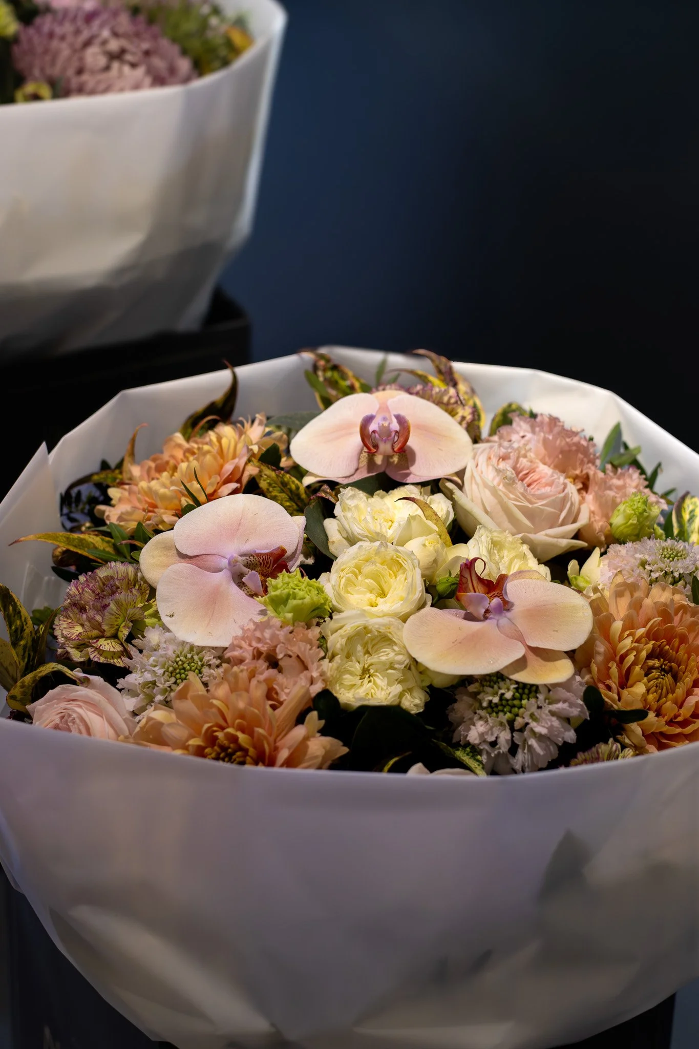 A bouquet of various pink, peach, and cream flowers in a white wrapping paper. Neill Strain, Harrods, Motcomb Street.