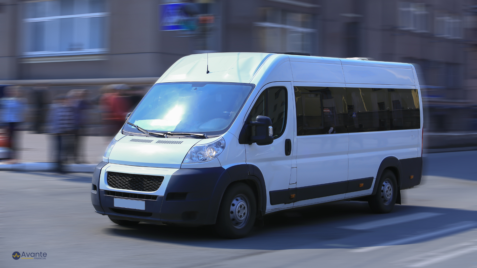 White passenger van driving on city street with blurred pedestrians in background.