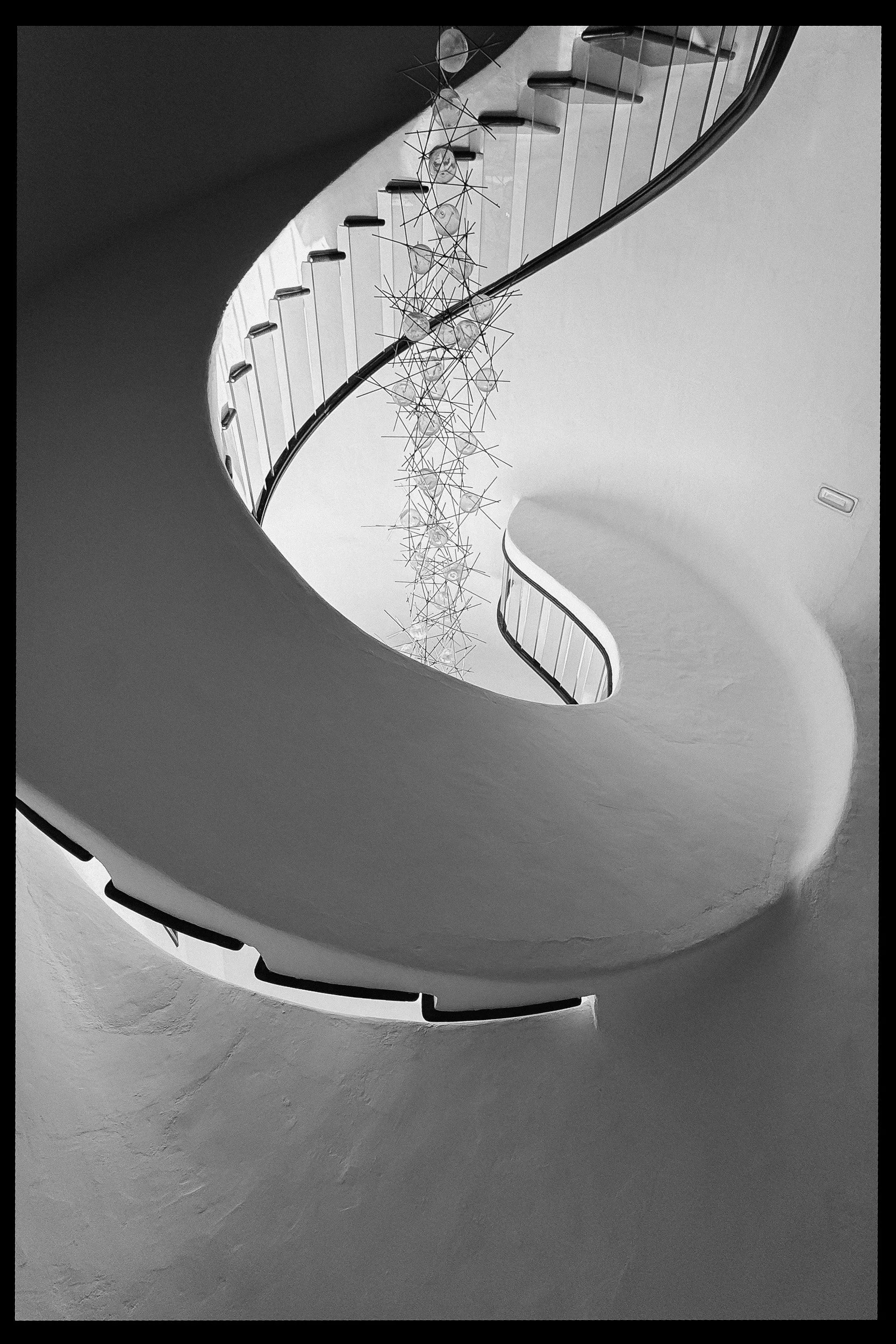 Spiraalvormige wenteltrap met een artistiek hangende decoratie aan het plafond, in zwart-wit.