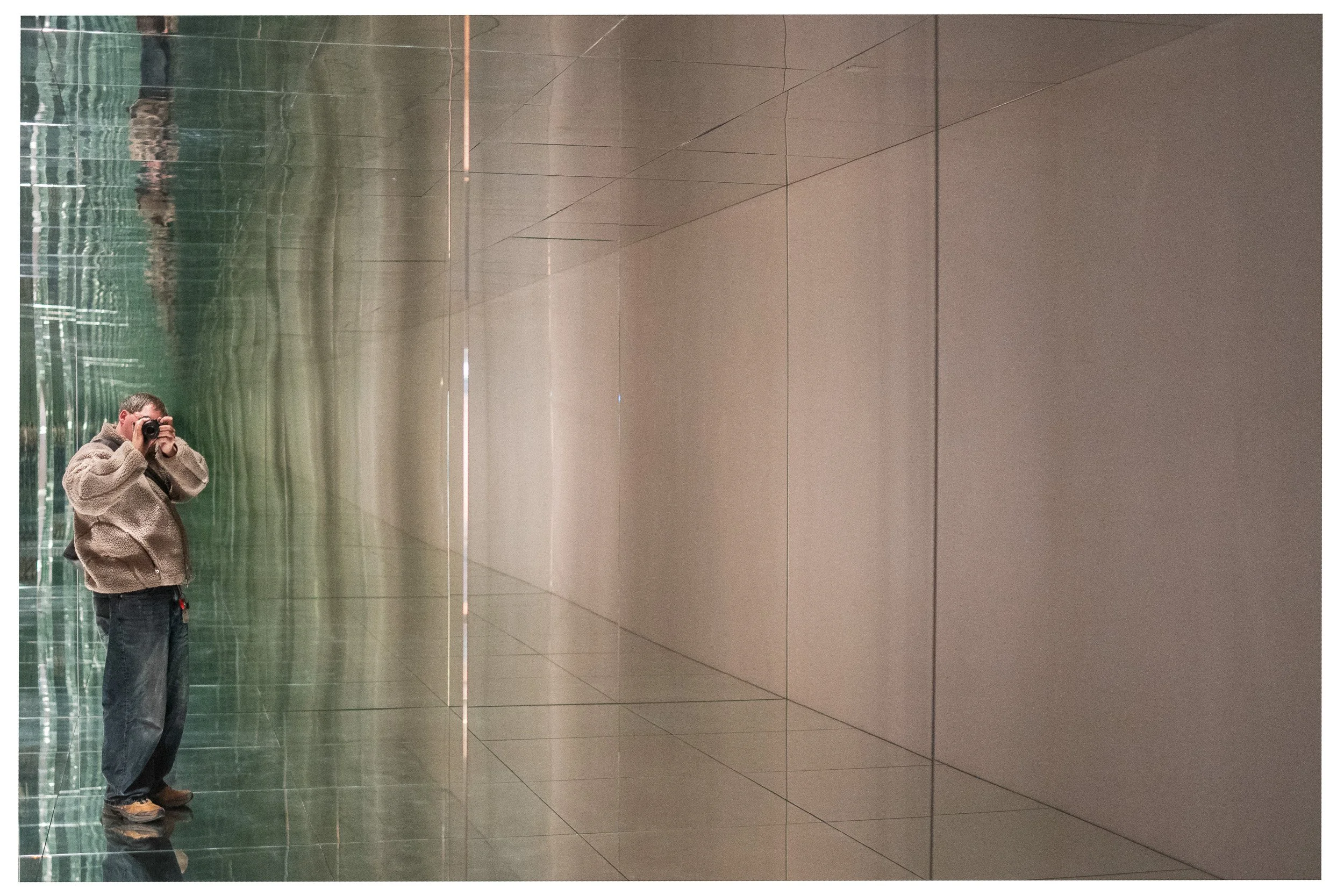 Persoon neemt foto in een hal met grote spiegels en betegelde muren.