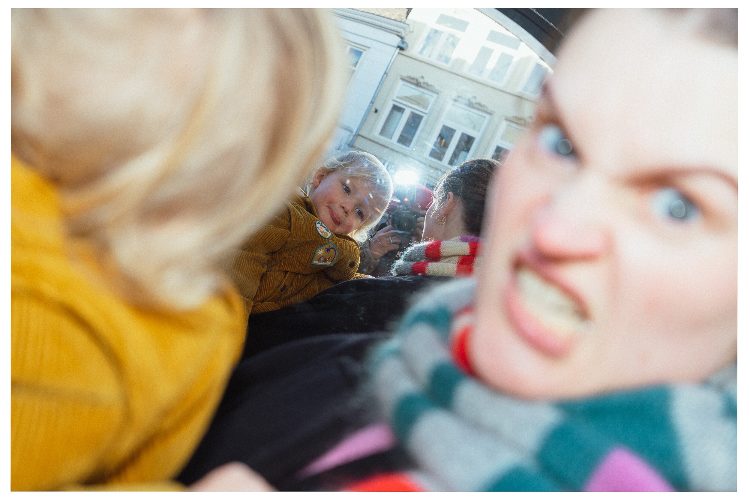 Close-up van kinderen, met enkele gezichten en kleding in focus, op een drukke locatie met historische gebouwen.