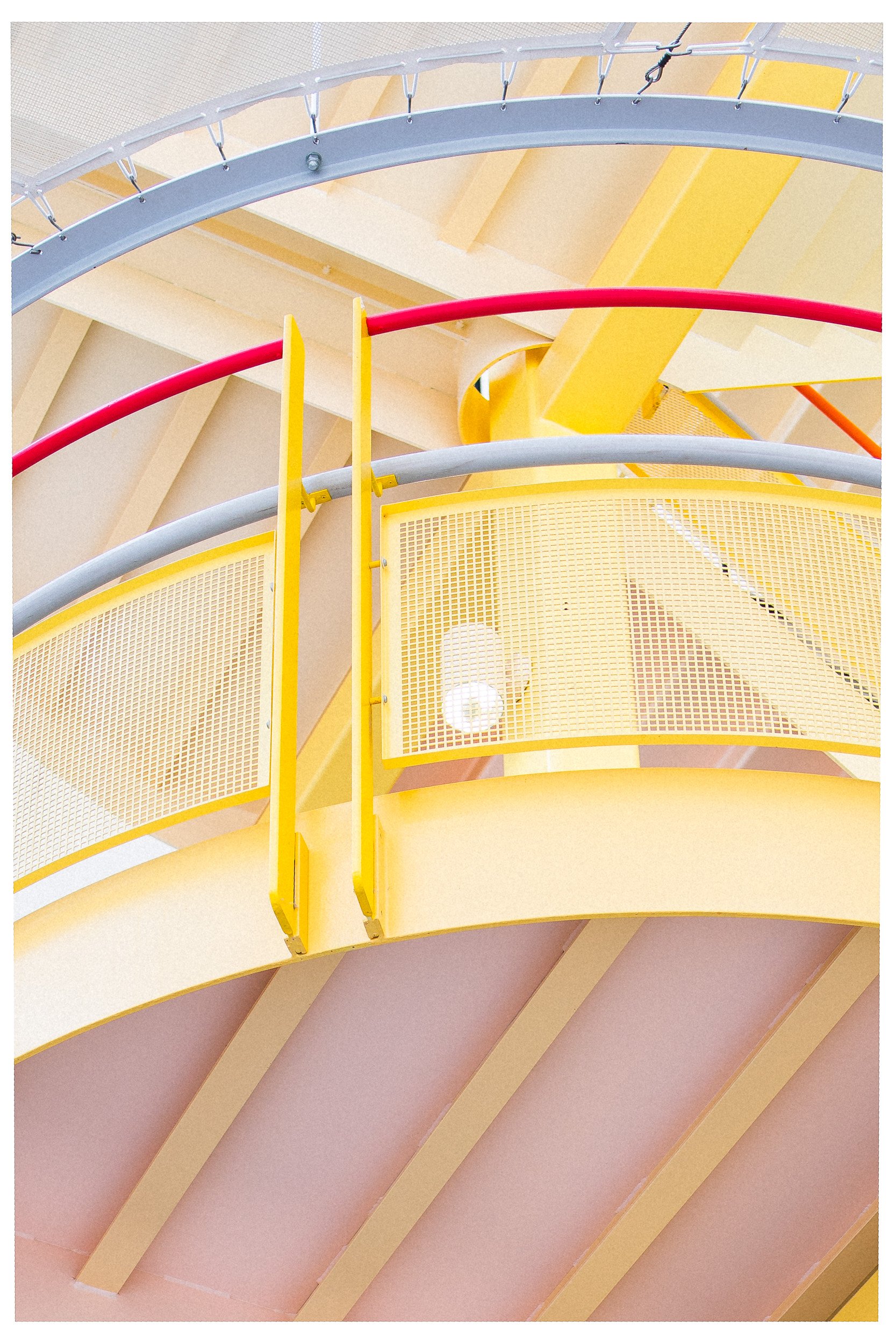 Close-up van een kleurrijke, moderne binnenstructuur met gele en rode metalen rails en gele geperforeerde panelen in een attractiepark, vermoedelijk een glijbaan of klimconstructie.