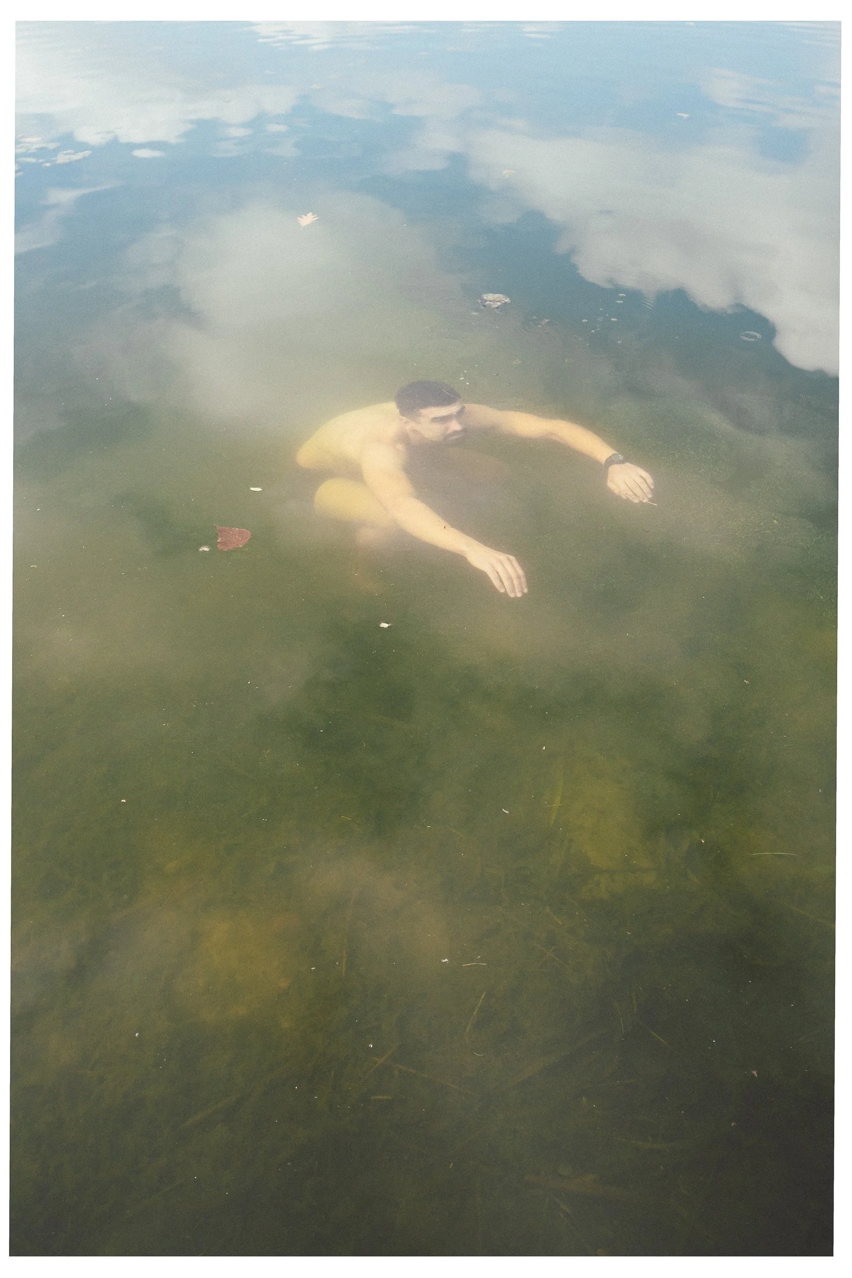 Man die onderwater zwemt in een groene plas met waterplanten en wat bladeren op het wateroppervlak.