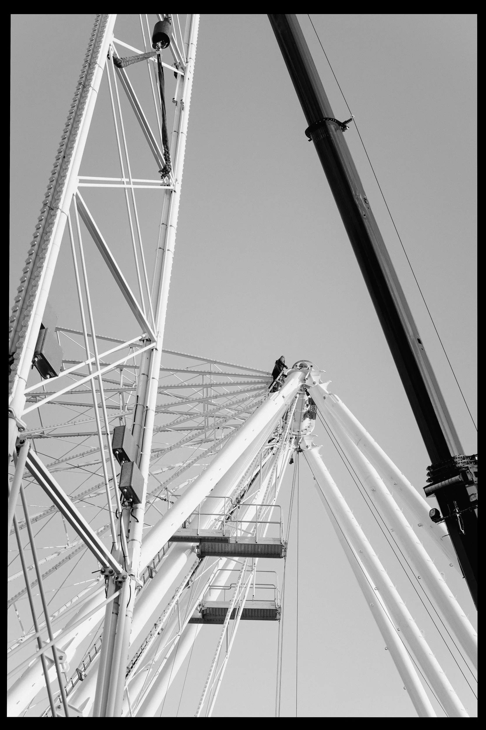 Zwart-wit foto van een grote draaimolen onder een heldere hemel. Verschillende stoelen en elementen van de attractie zijn zichtbaar, met iemand die op de top staat.