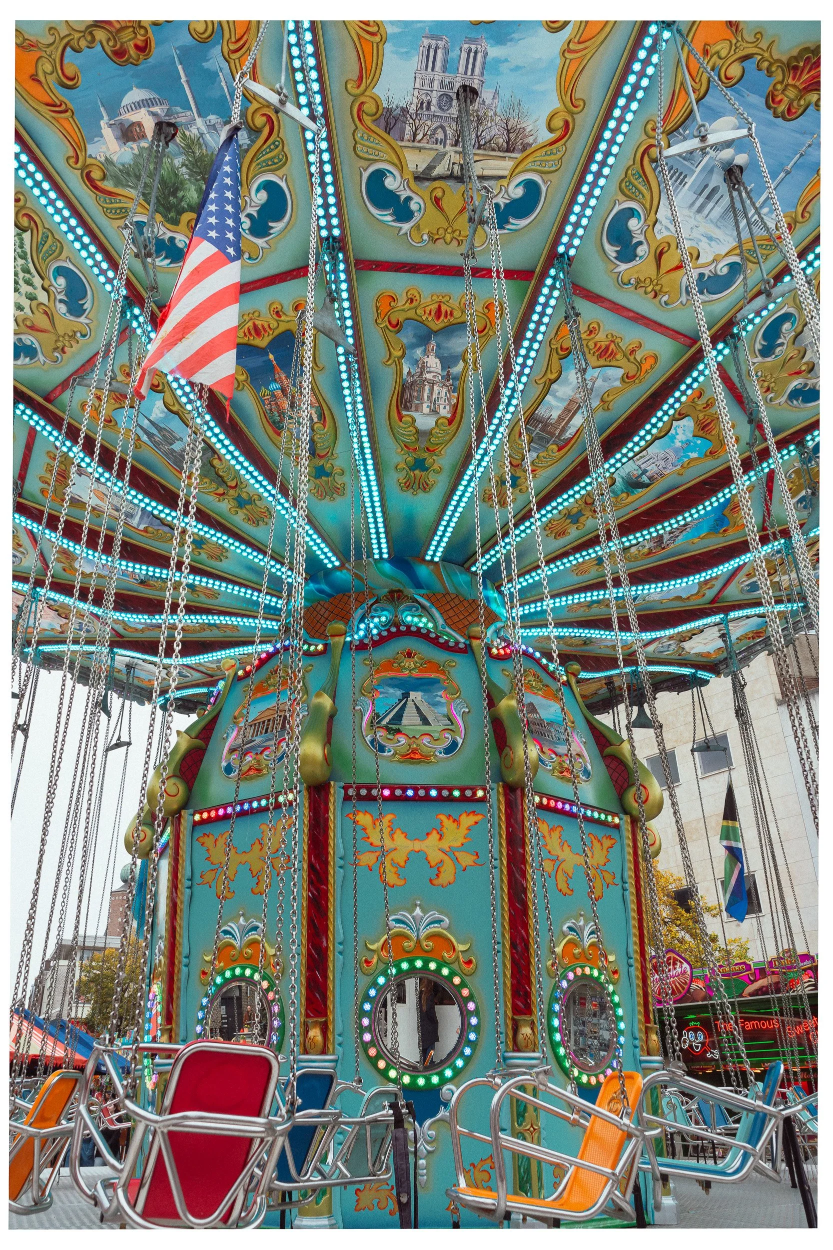Een kleurrijke draaimolen met stoeltjes, decoratief versierd en versierd met schilderijen van beroemde gebouwen, en een Amerikaanse vlag hangt aan de bovenkant.