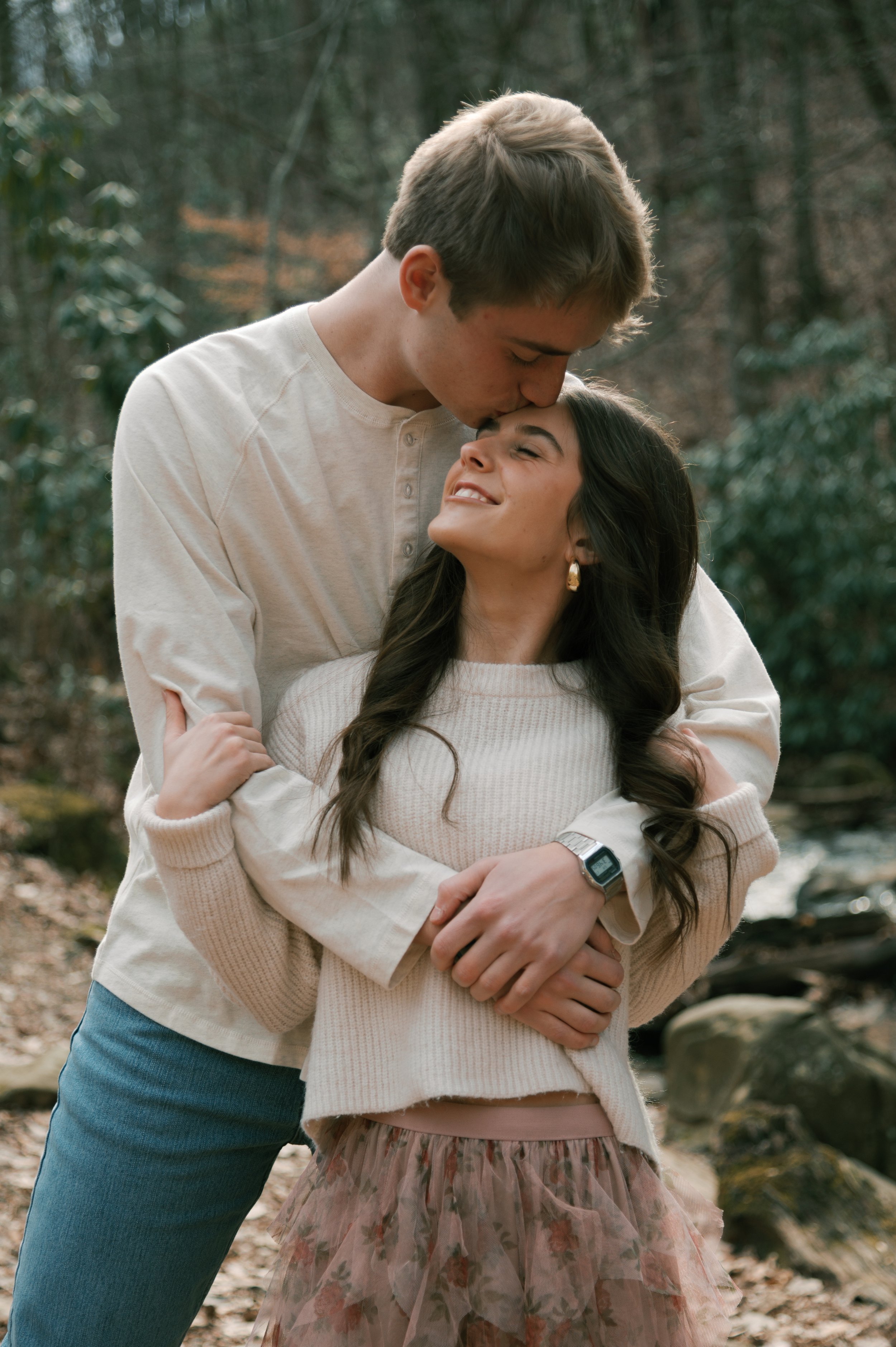 Couple in warm embrace, male kissing female on forehead happy to be engaged.