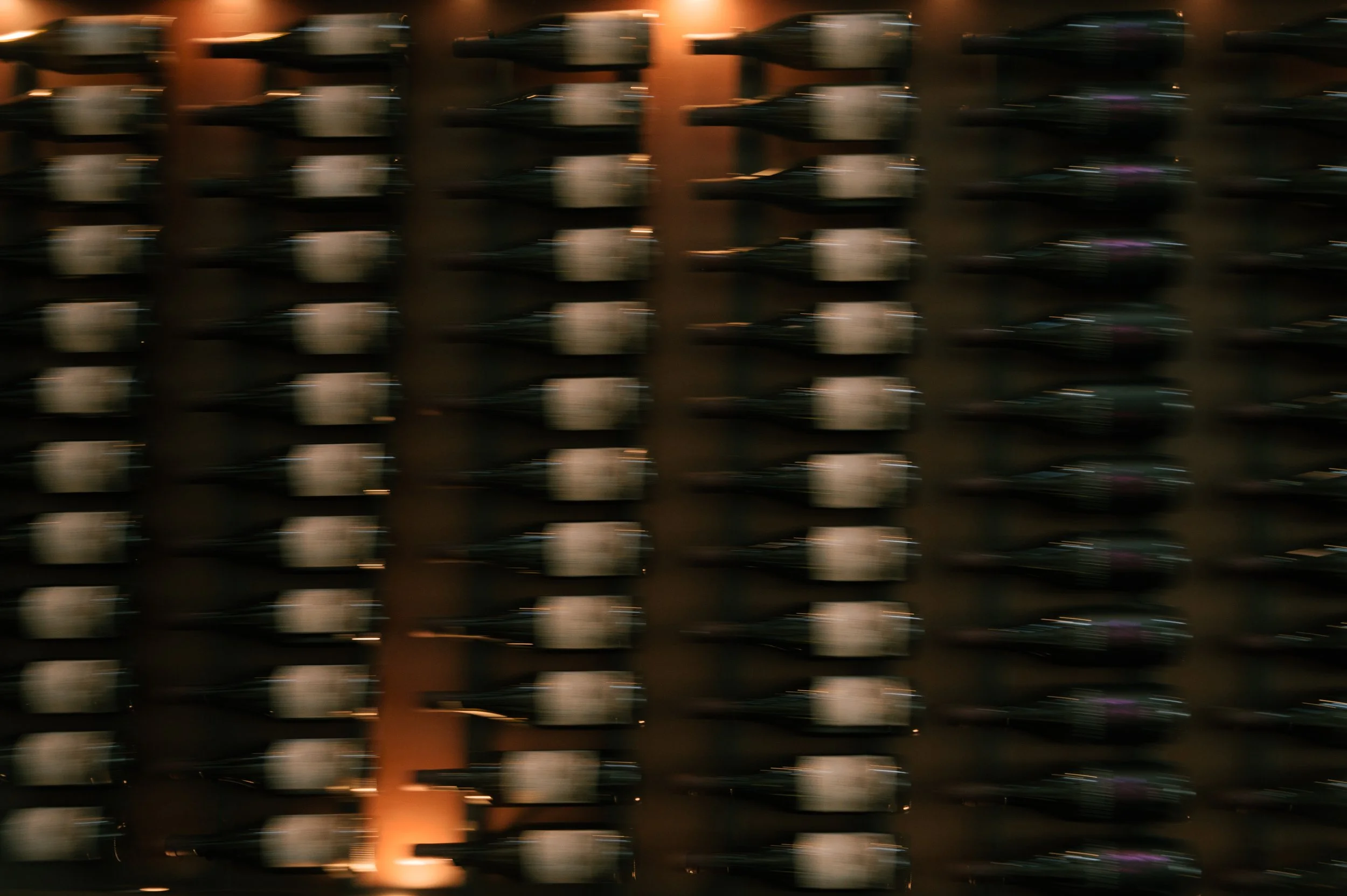 Motion-blurred image of a wall filled with rows of wine bottles in a wine cellar