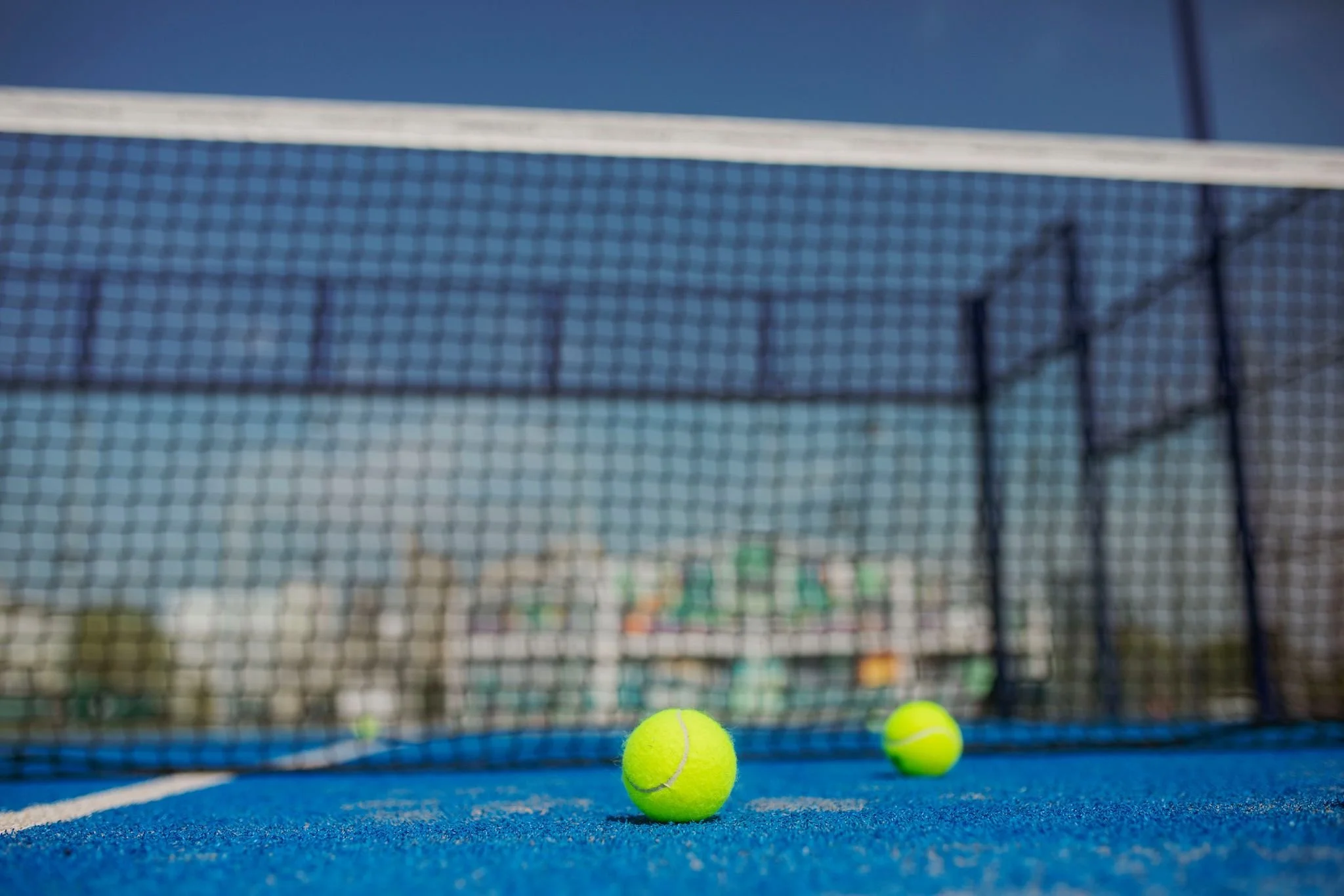 Två tennisbollar på en blå tennisbana framför en tennisnät.