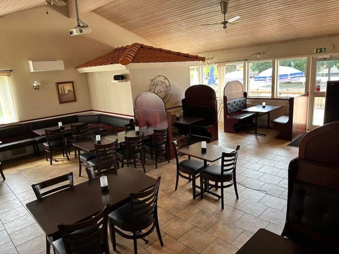 Interiör av ett tomt restaurangkafé med flera stolar och bord, soffor och högbås, stora fönster, trägolv och en träsample på taket.