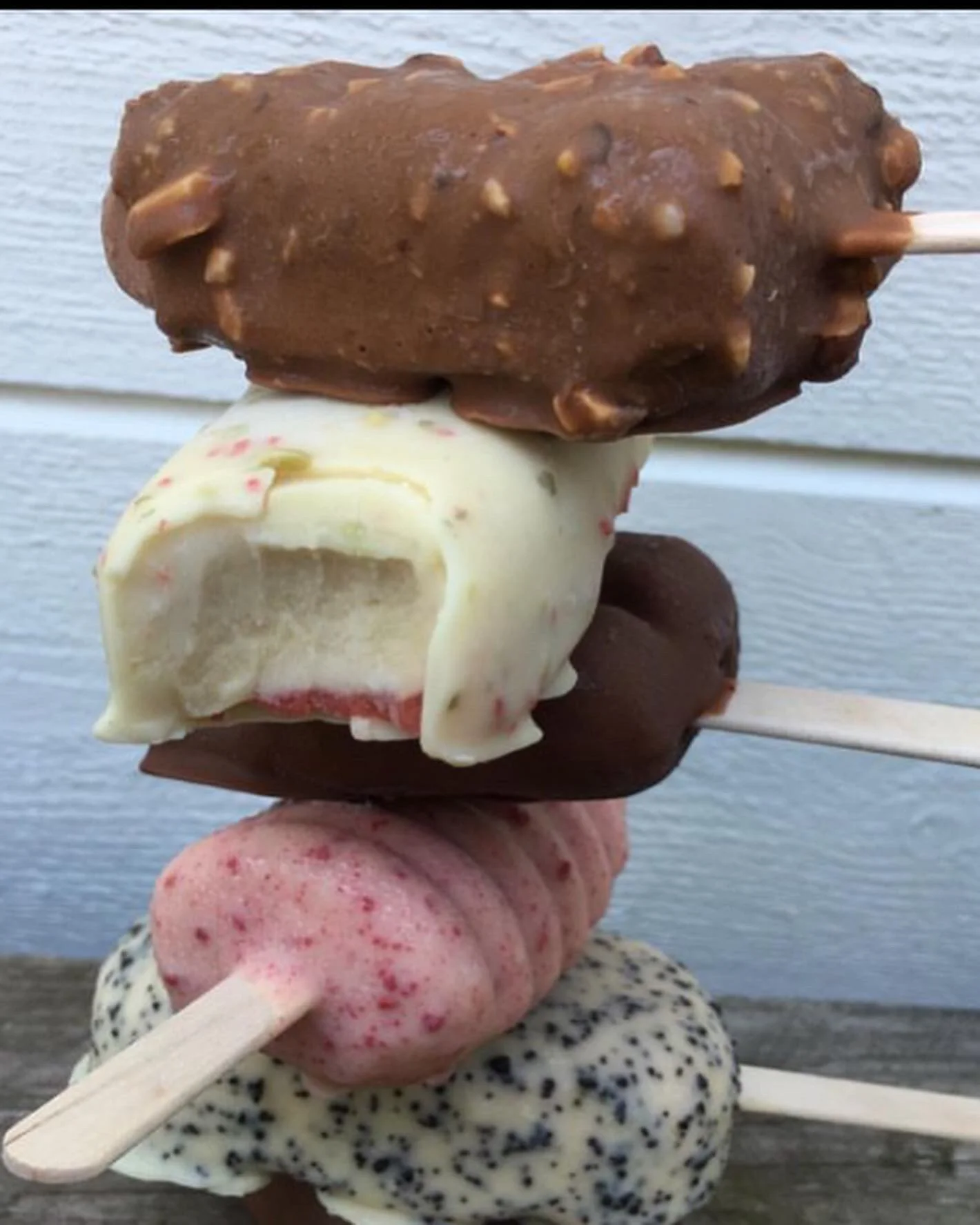 Fyra glasspinnar med olika glassar, staplade på varandra framför en blå trävägg.