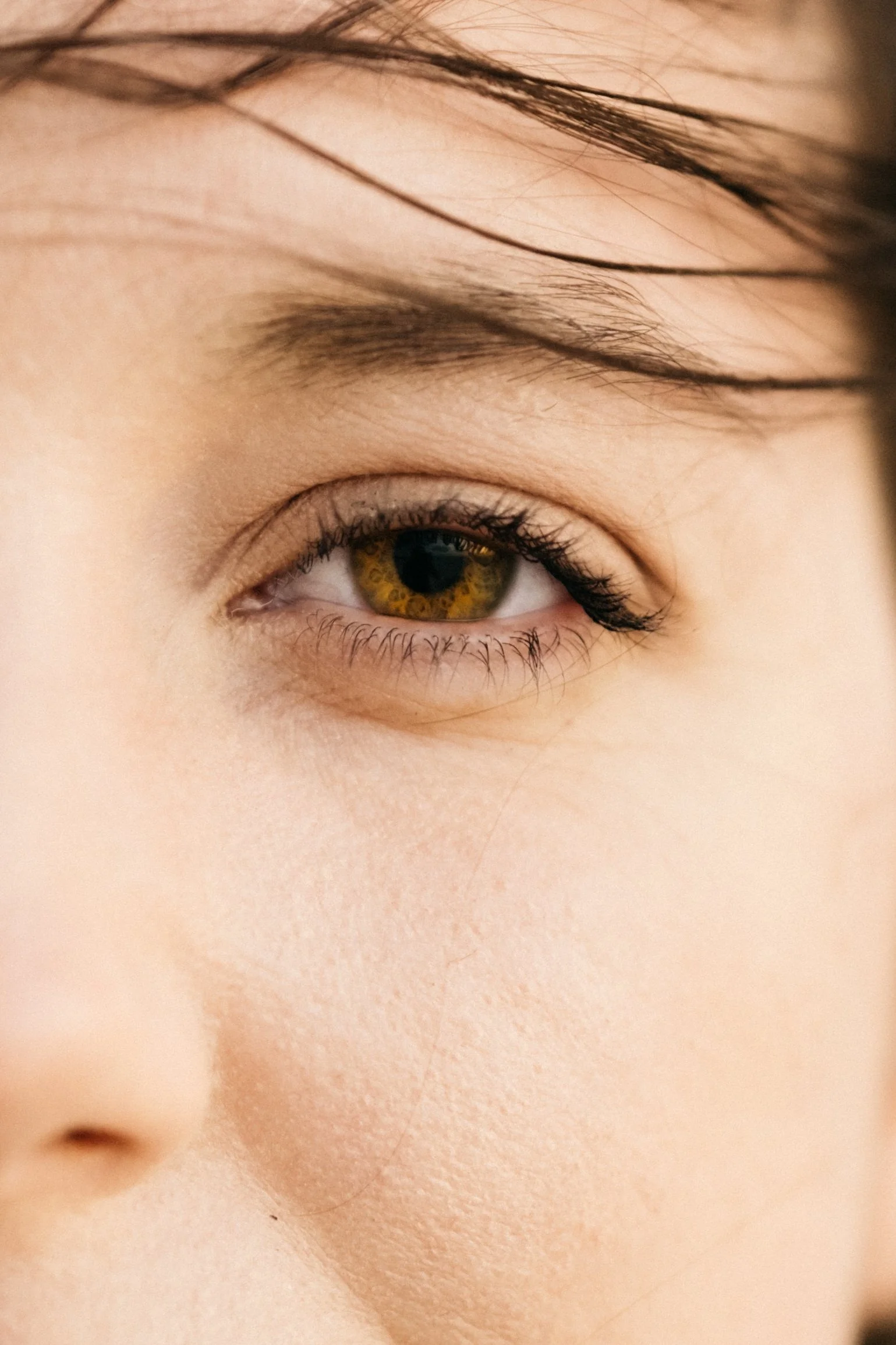 Close-up of a person's eye with brown iris and long eyelashes, with light skin and black hair.