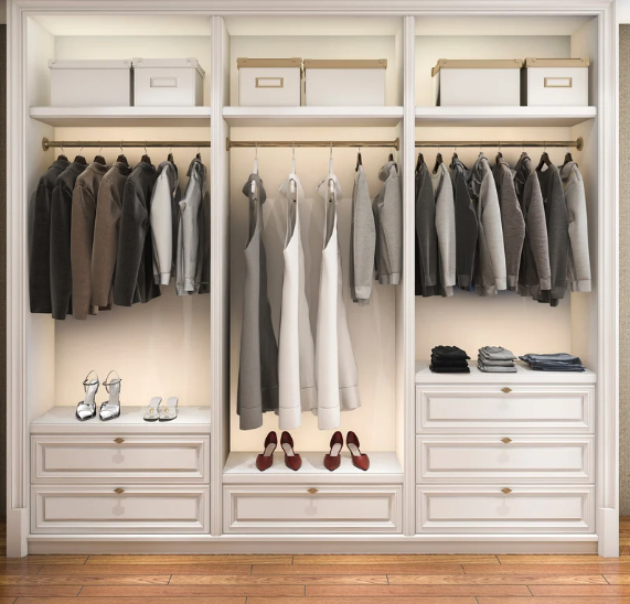A neatly organized white closet with three sections. The left section has hanging gray, black, white, and brown jackets with a pair of heels and sandals on a shelf below. The middle section has hanging white and gray dresses with red shoes on the floor. The right section has hanging gray and black clothing with folded clothes on the shelf below.