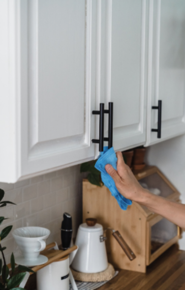 Person cleaning cabinet handles with a blue cloth in a kitchen.
