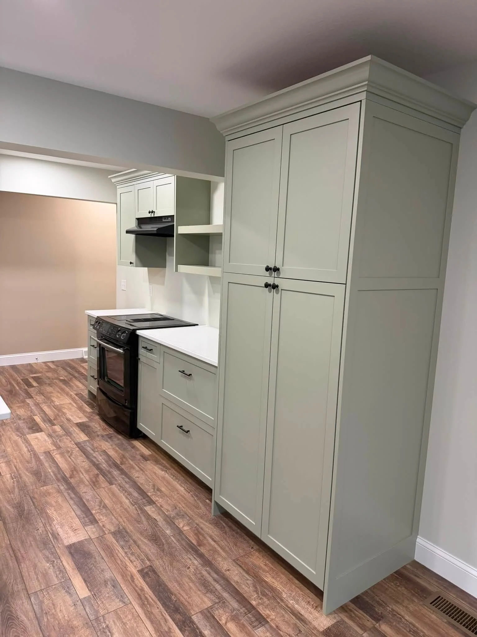 Interior view of a kitchen with light green cabinets, black stove, wood flooring, and gray walls.