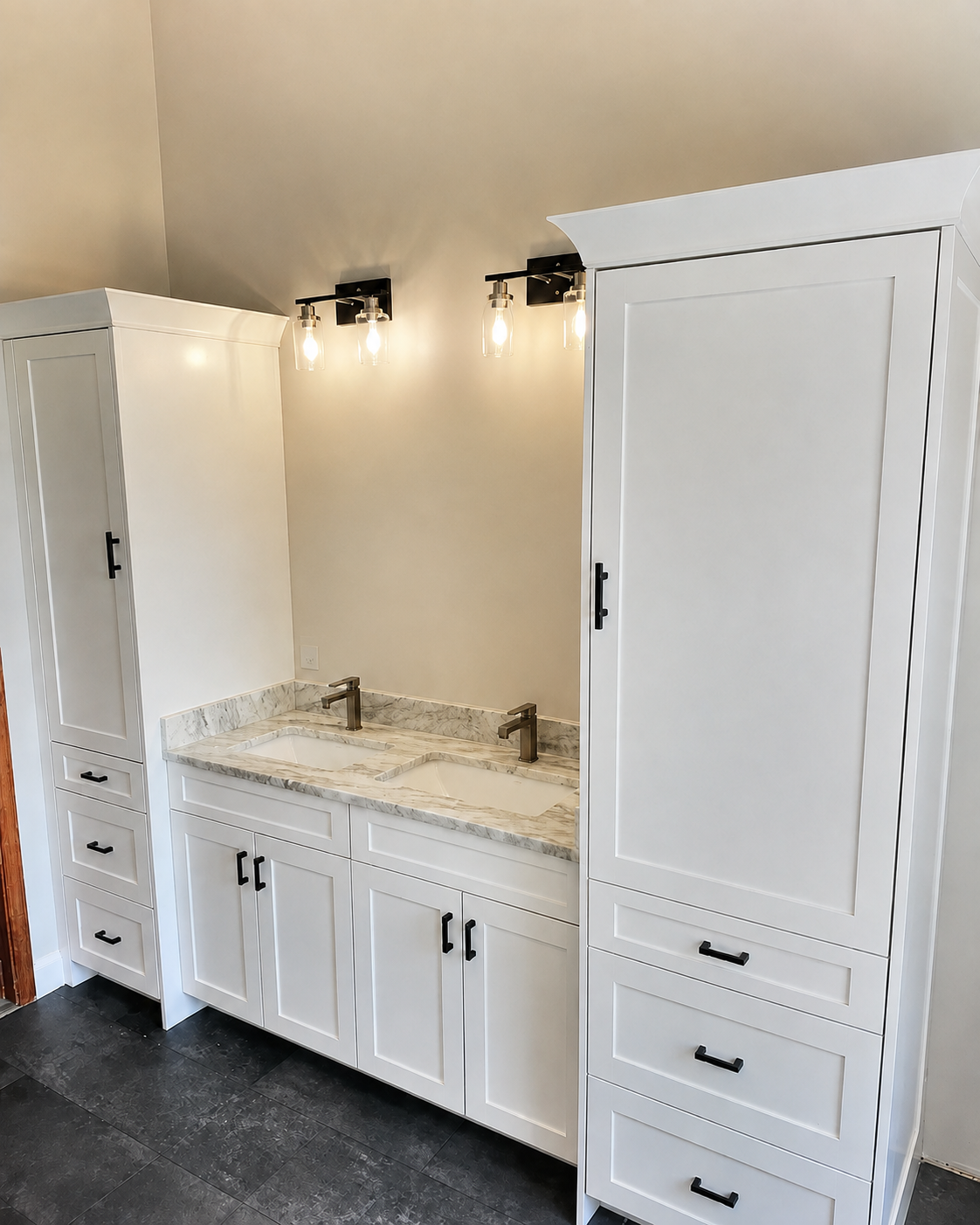 A modern bathroom vanity with dual sinks, a marble countertop, white cabinets with black handles, and a large mirror with contemporary light fixtures.