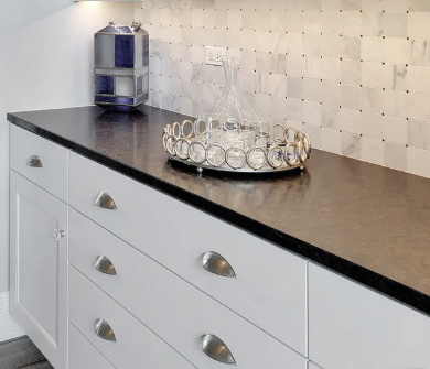 A black countertop with white cabinets underneath, a blue and white storage rack, and a decorative tray with a glass decanter.