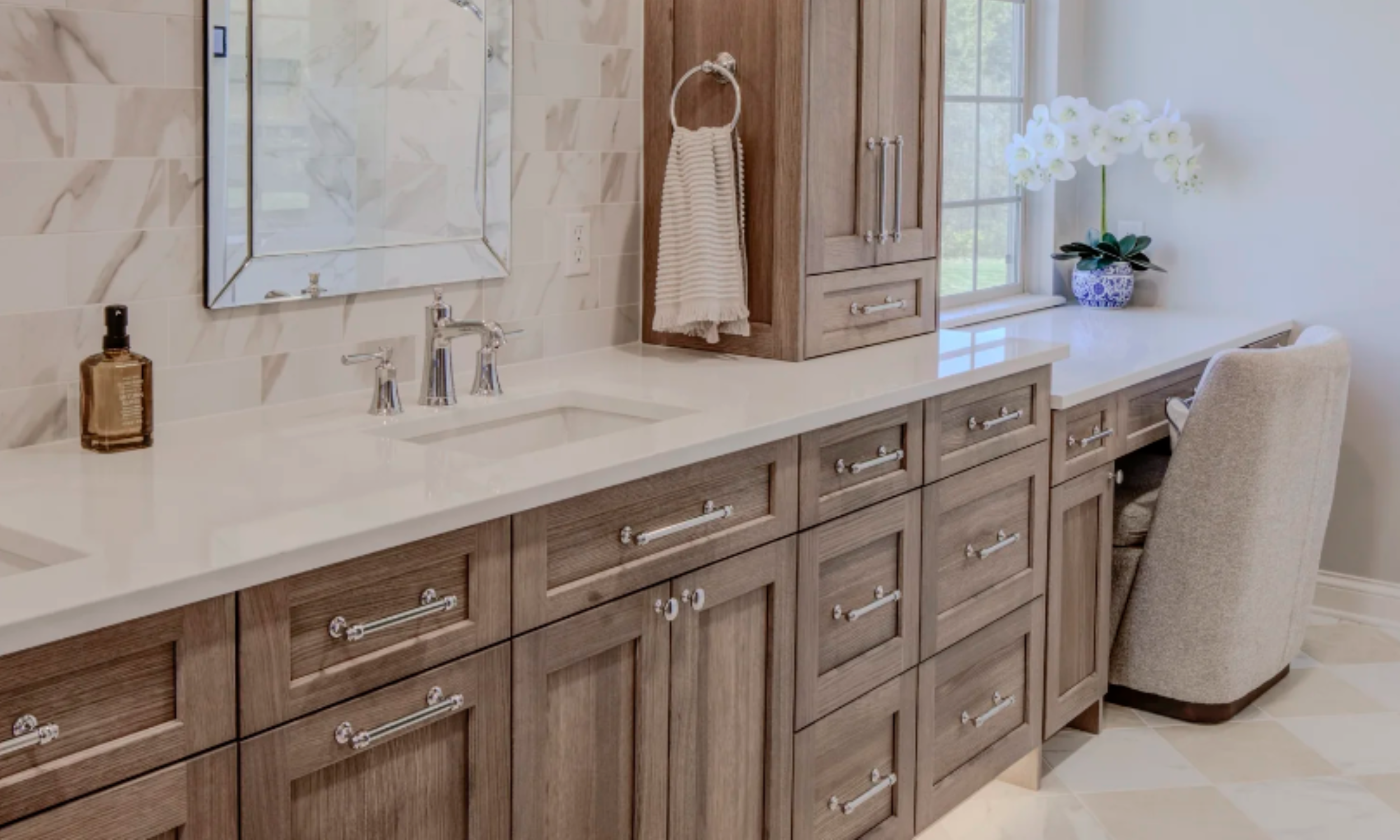 Luxury bathroom custom weathered-grain stained wood vanity with white quartz countertops, a matching vertical linen tower cabinet, and an integrated drop-down makeup vanity desk with a cushioned chair.