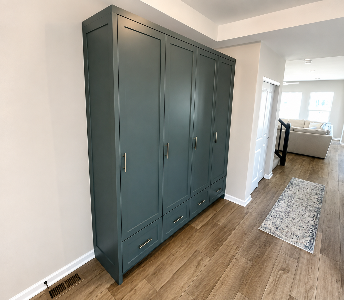 A teal-colored bedroom wardrobe with gold handles, positioned against a white wall on a wooden floor and a beige area rug nearby.