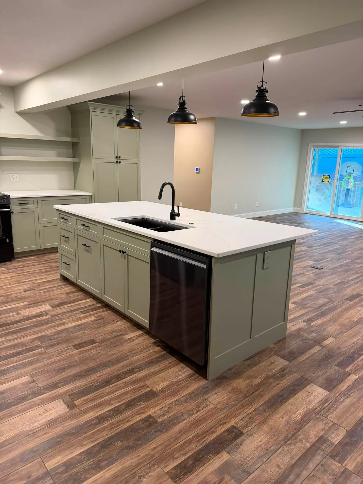 Kitchen with a large island, black sink, pendant lights, cabinets, and hardwood floors.