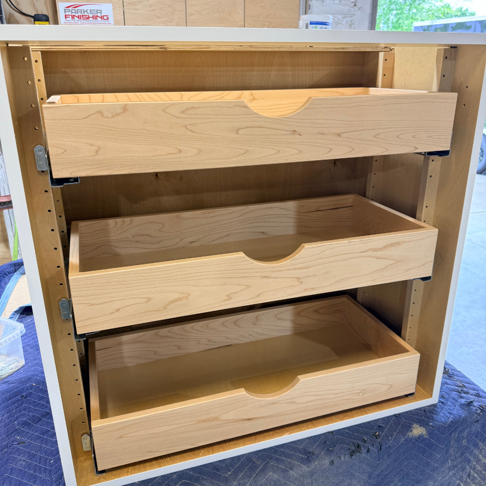 Custom cabinetry unit featuring three stacked, wooden pull-out rollout drawers with scoop-cut handle pullouts, showcasing natural maple wood box craftsmanship.
