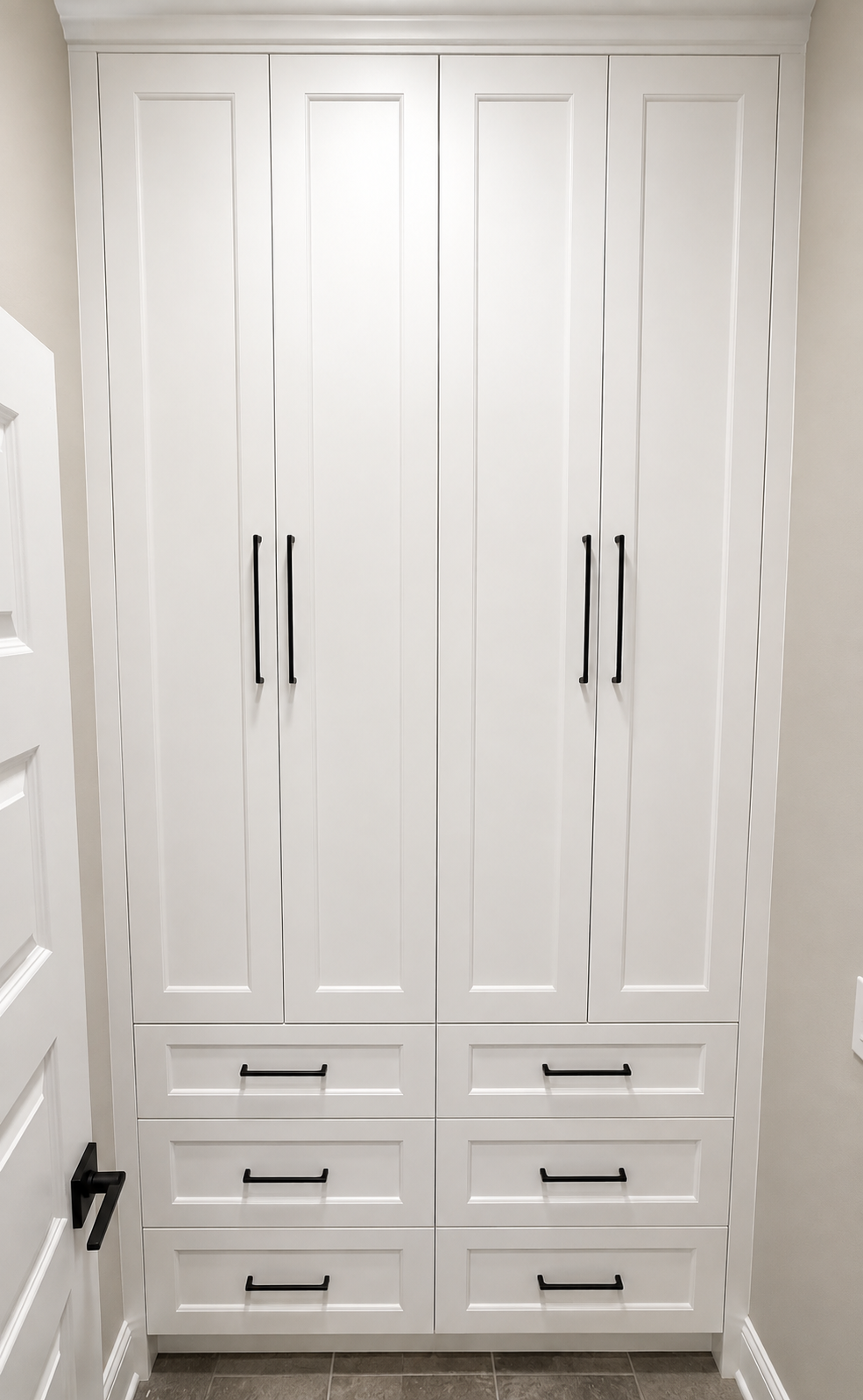 White built-in closet with four doors and three drawers at the bottom, all with black handles, located in a modern room.