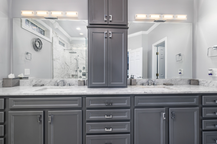 Bathroom vanity with gray cabinets, marble countertop, and mirror, with a shower visible in the background.