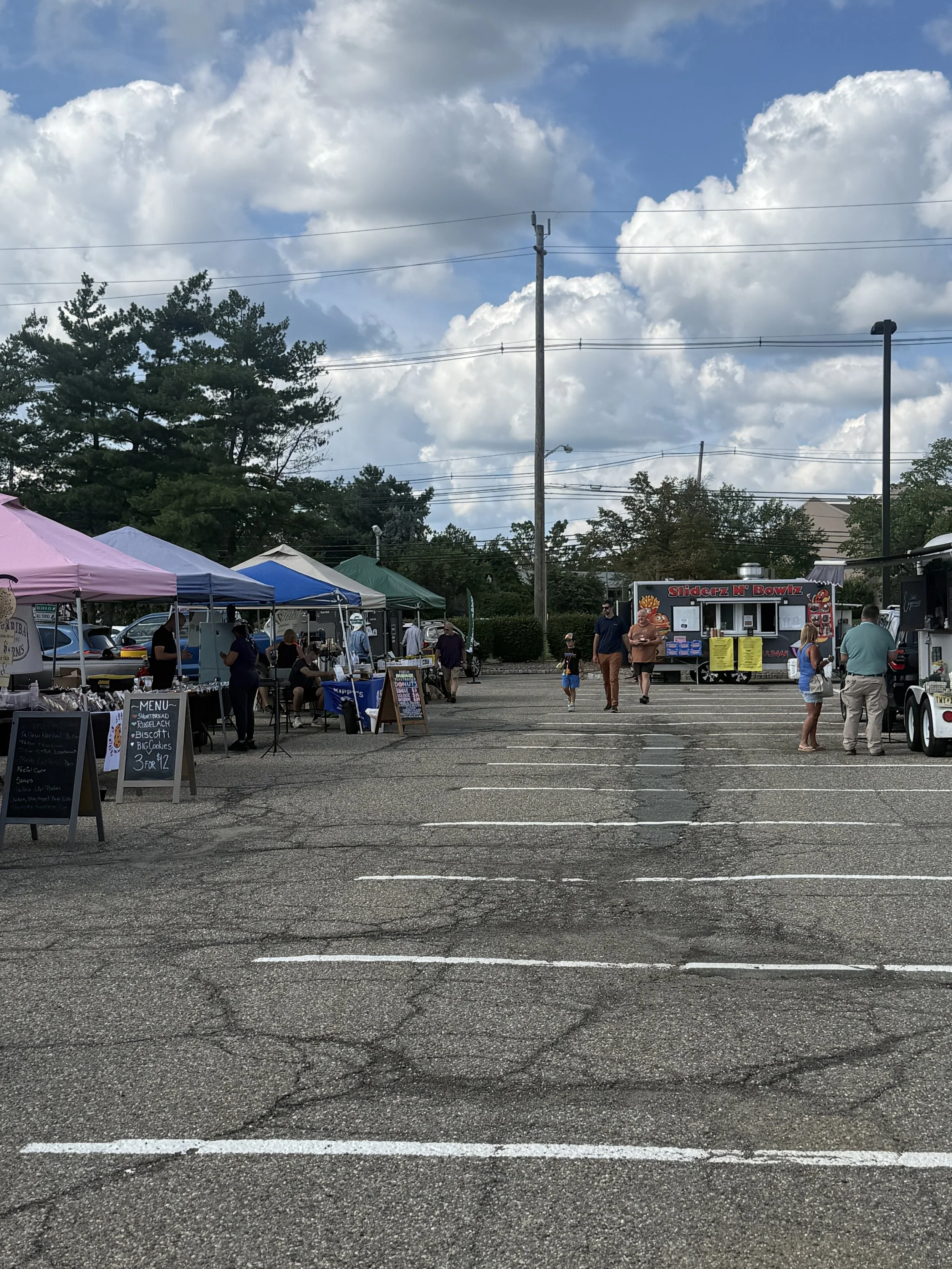 Outdoor market with vendor tents, people shopping, and food truck, under partly cloudy sky. Parsippany Farmers market by Hear Here Events 2026 season