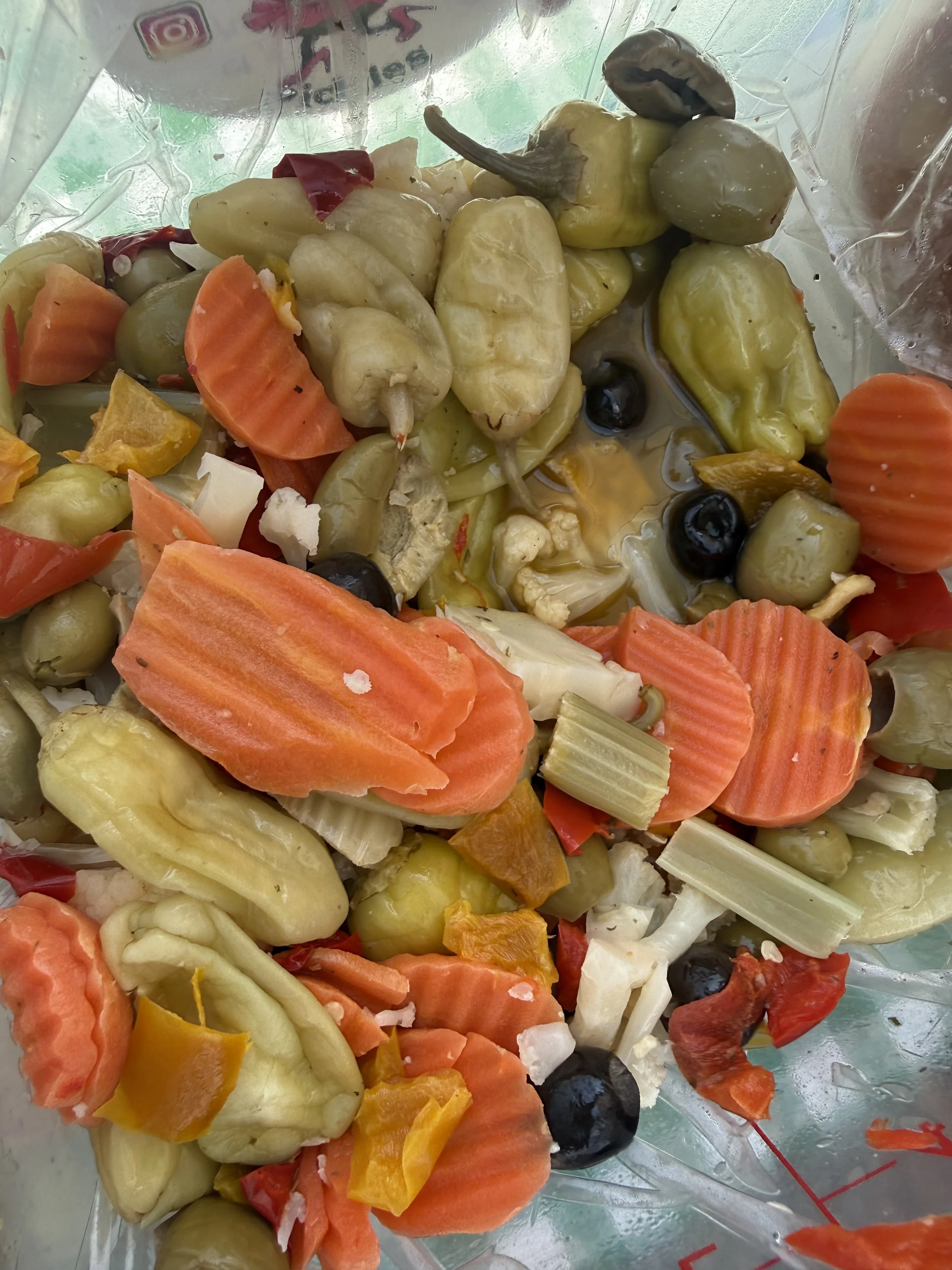 A mixture of pickled vegetables including green olives, carrots, cauliflower, red bell peppers, and other assorted vegetables in a plastic bag. Parsippany Farmers market by Hear Here Events 2026 season