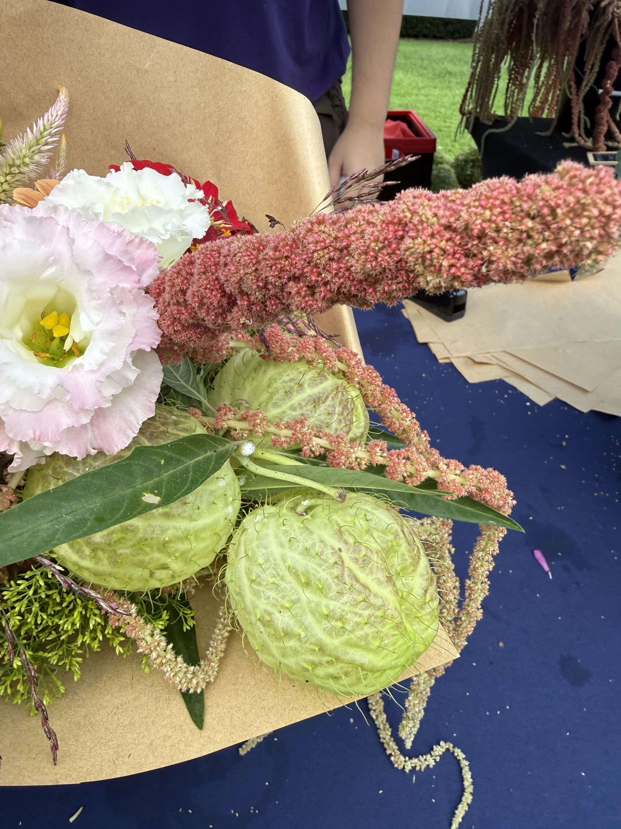 Arrangement of various flowers including pink astilbe, white and pink lisianthus, and greenery on a tan paper background. Howell Farmers market by Hear Here Events 2026 season