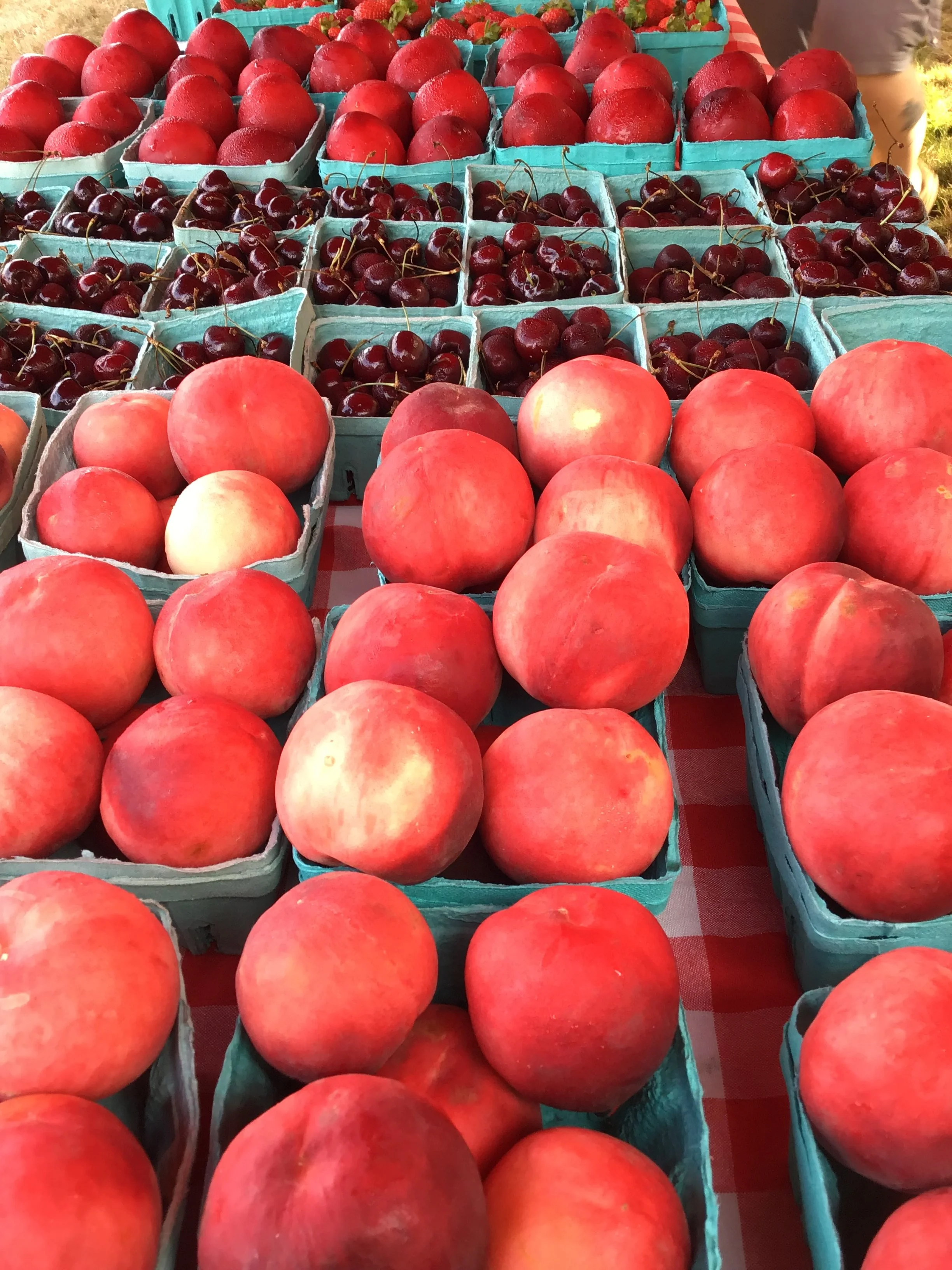 A display of fresh peaches and cherries in individual green containers at a fruit stand. Howell Farmers market by Hear Here Events 2026 season