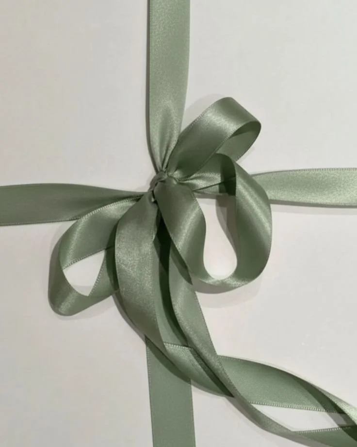 Close-up of a white gift box wrapped with light green satin ribbons tied into a bow.