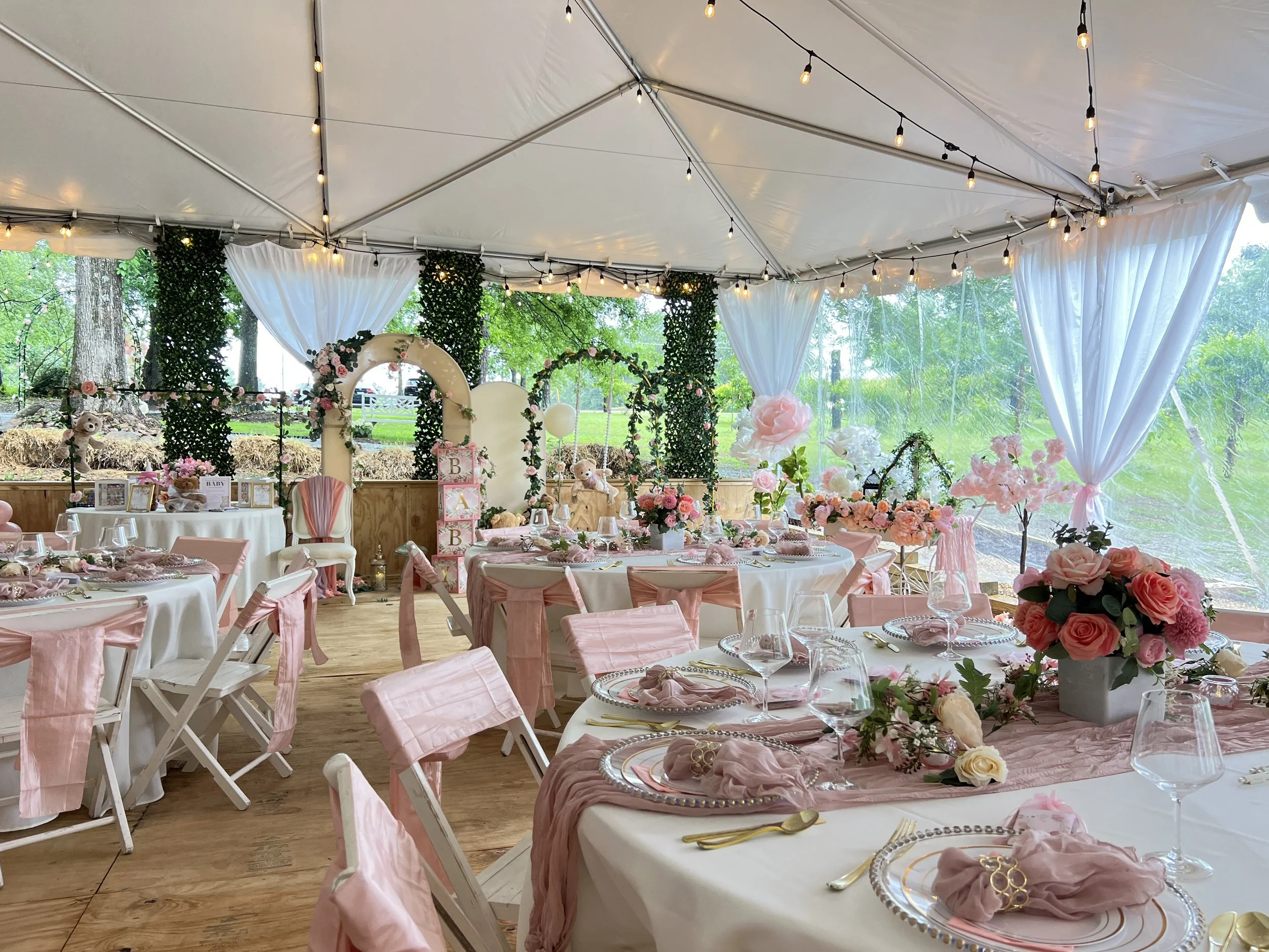 A decorated outdoor event tent with pink and white themed tables and floral arrangements, set for a celebration or wedding reception.