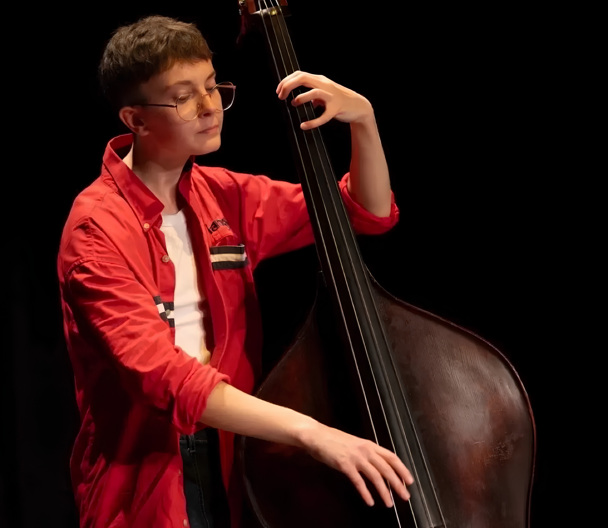 A young, white person with short hair and glasses plays a cello