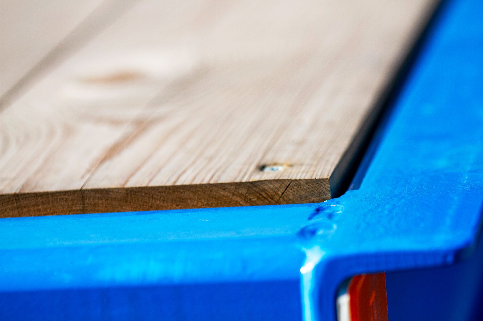 Nahaufnahme eines Holzbretts auf einer blauen Oberfläche, mit sichtbaren Holzmaserungen und Knoten.