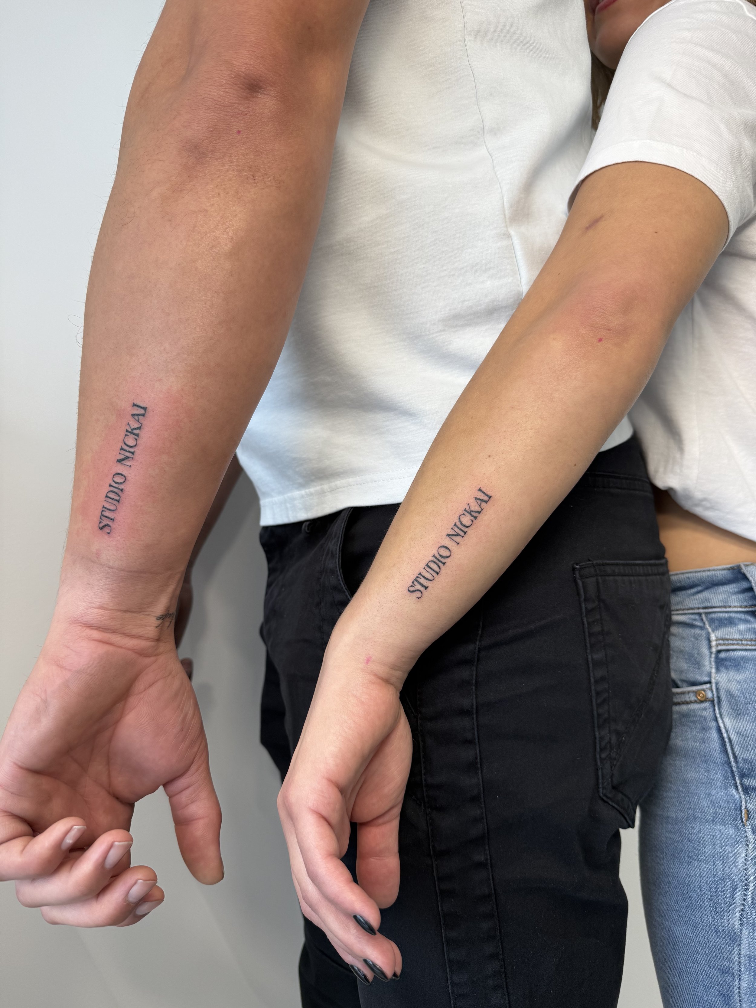 Mensen die elkaars vingers vasthouden, met tattoos op de onderarmen met de tekst 'STUDIO NICKAL'