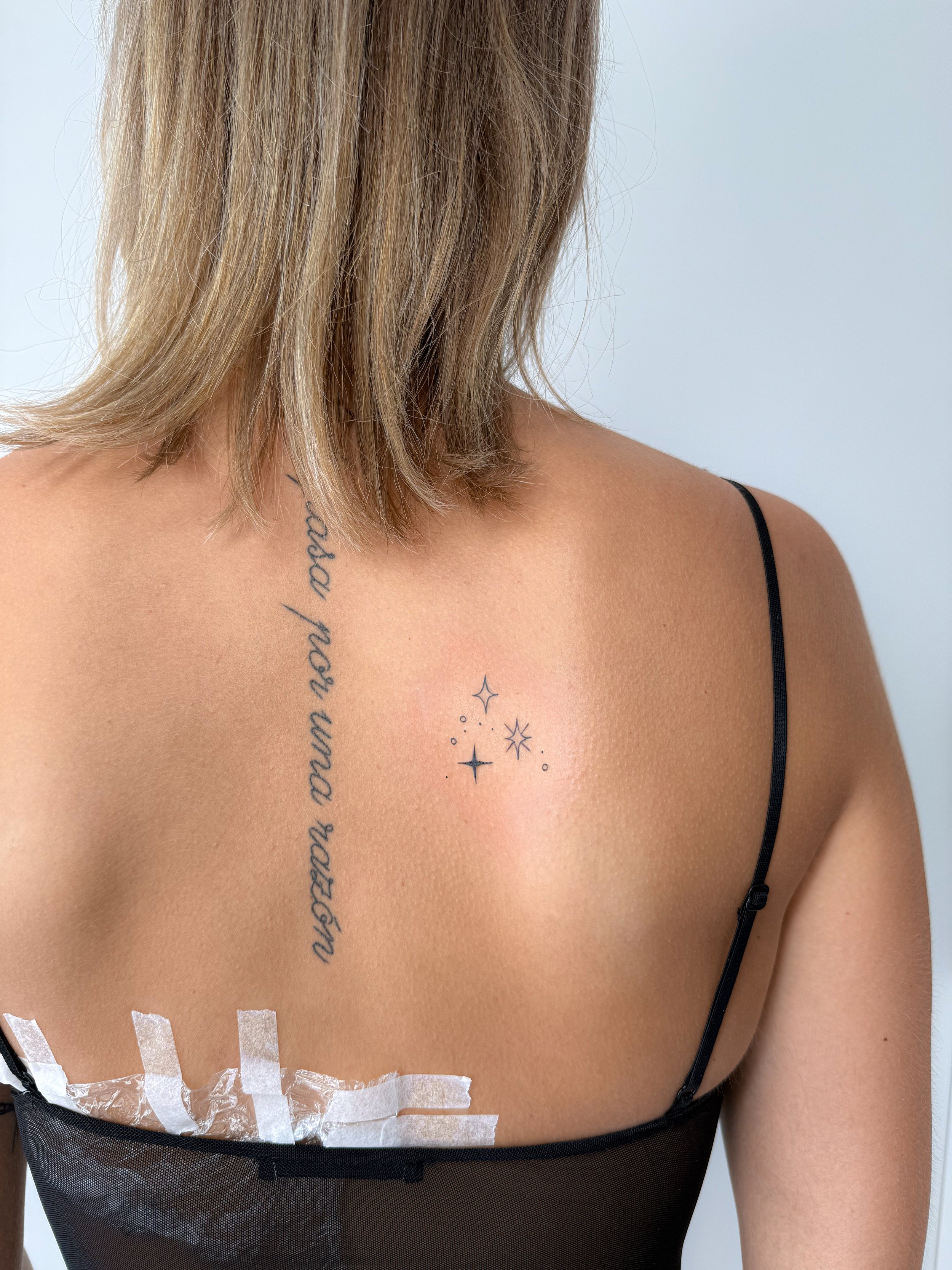 Close-up van een schouder en borst met een tattoo en een zwart hemd, met vaseline en pleisters op de onderkant van de borst.